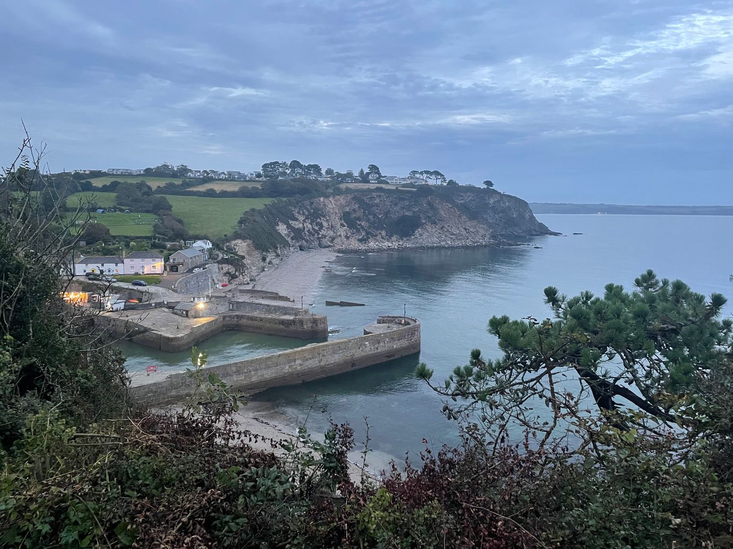 A coastal harbor with a stone pier and small buildings near the water at Sea Drift in Carlyon Bay near Charlestown