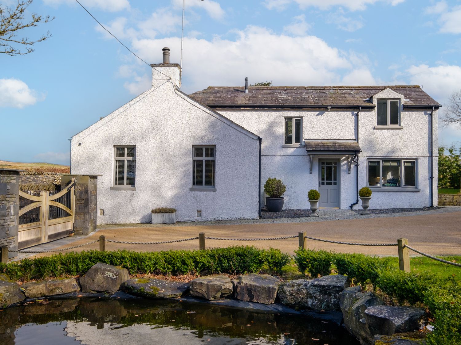 A white two-story house with a gravel driveway and plants near a small pond at Gate House in Killington near Sedbergh