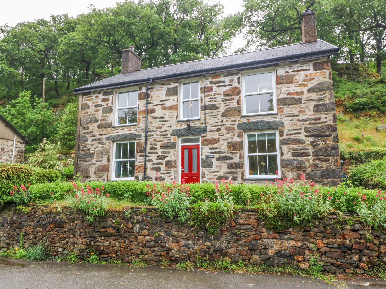 A stone house with red front door and flower beds at Ty Capel Bethania Nant Gwynant