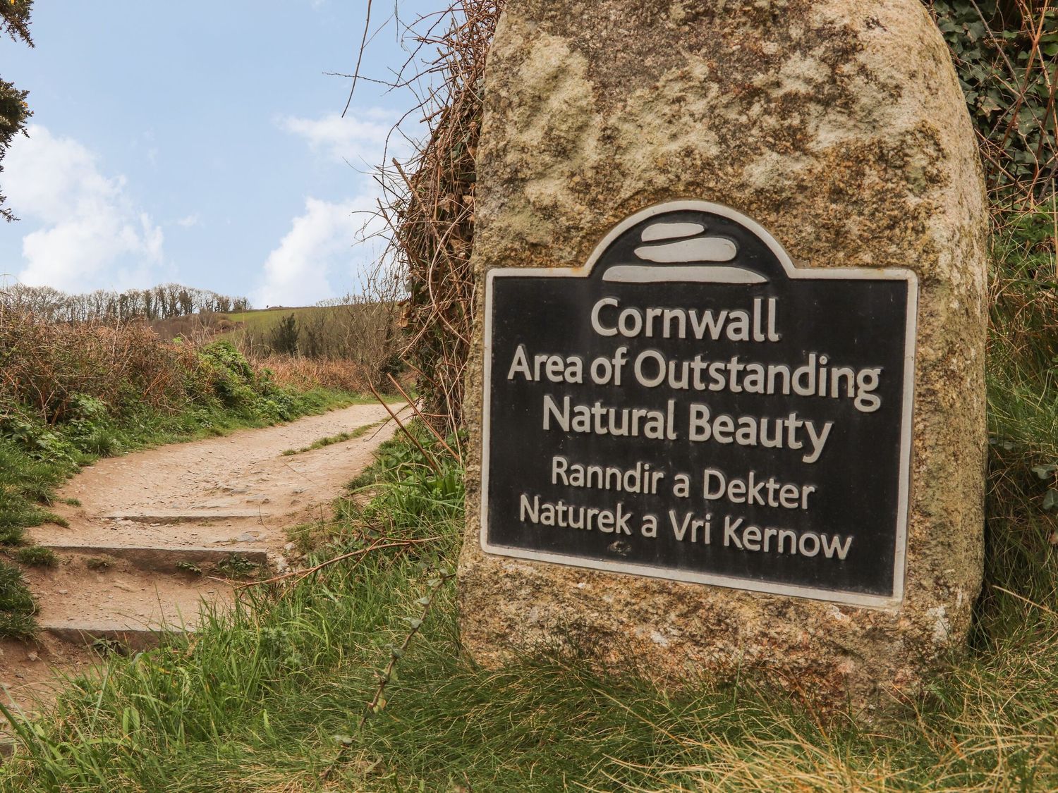 A stone sign marking Cornwall Area of Outstanding Natural Beauty next to a dirt path with grass and bushes at Lakeside in Falmouth