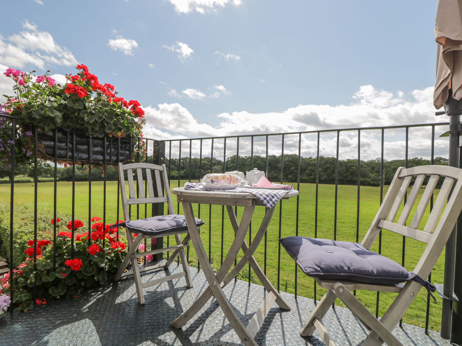 A balcony with two wooden chairs and a table set for tea overlooking a green field at The Coach House in Newent