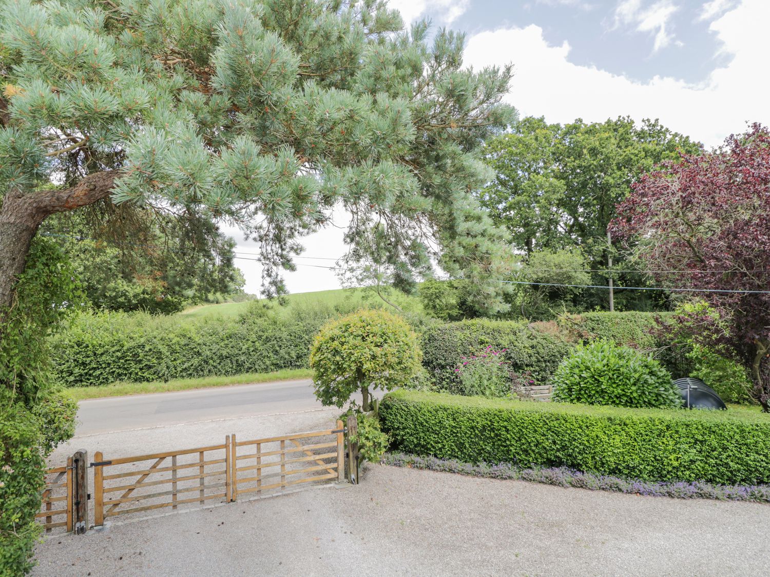 A wooden gate opening to a road with hedges trees and bushes surrounding the area at The Coach House in Newent