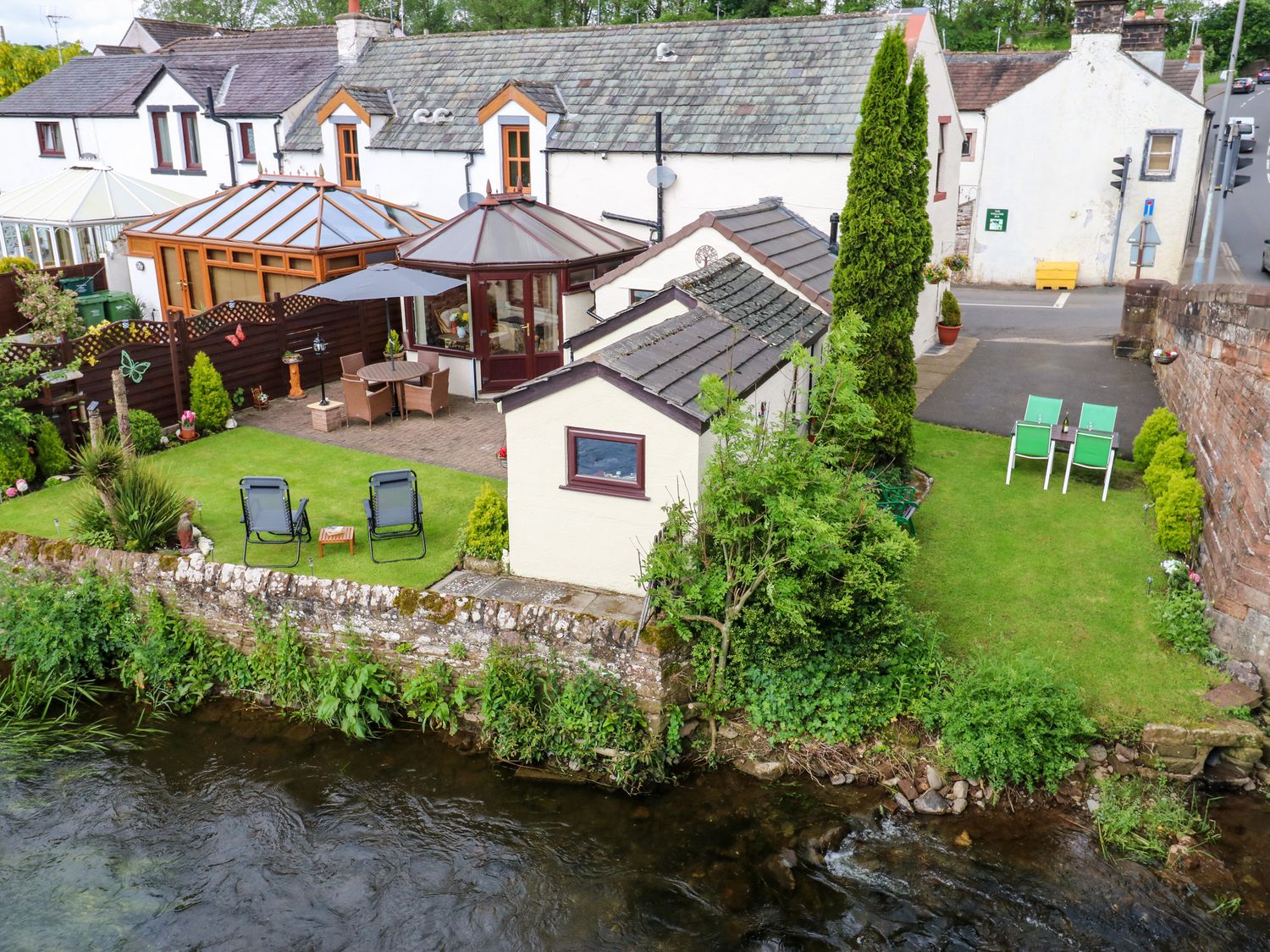 A riverside garden with outdoor seating and a patio next to a row of white cottages at River Cottage in Eamont Bridge