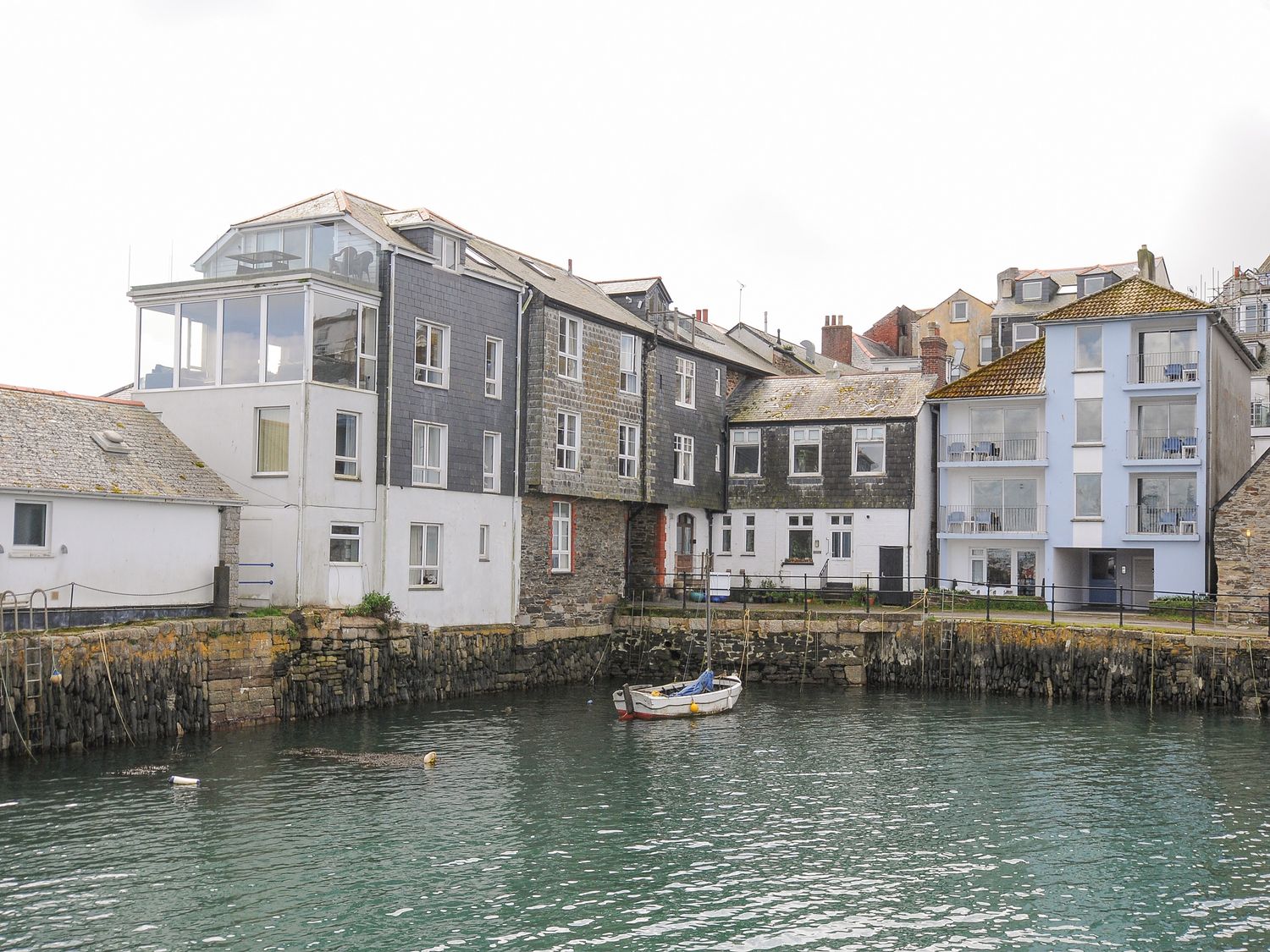 A small boat in a harbor next to buildings with stone and white walls at Zawn Haven - Waterfront House in Falmouth
