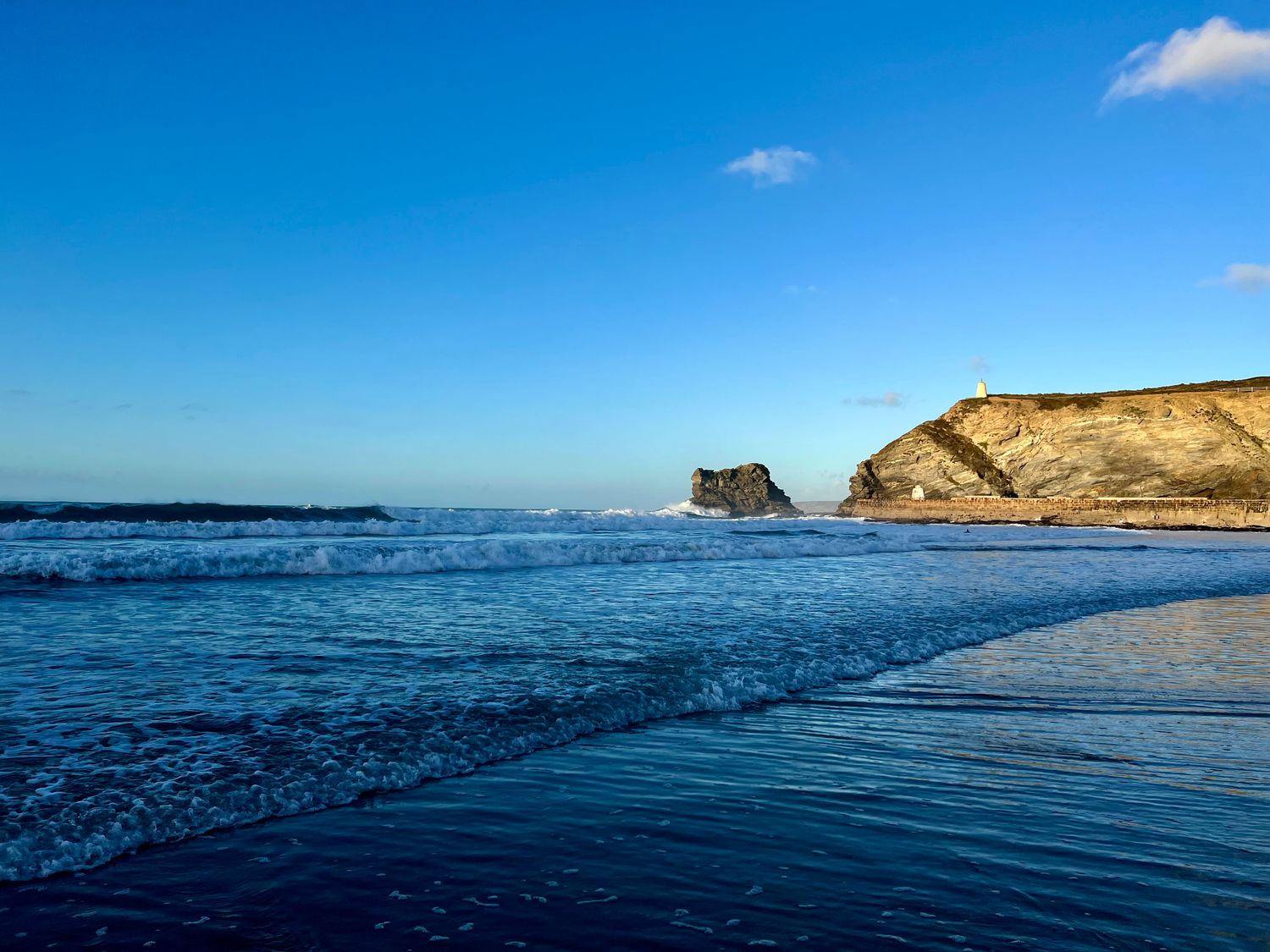 A beach with waves and a rocky cliff under a clear blue sky