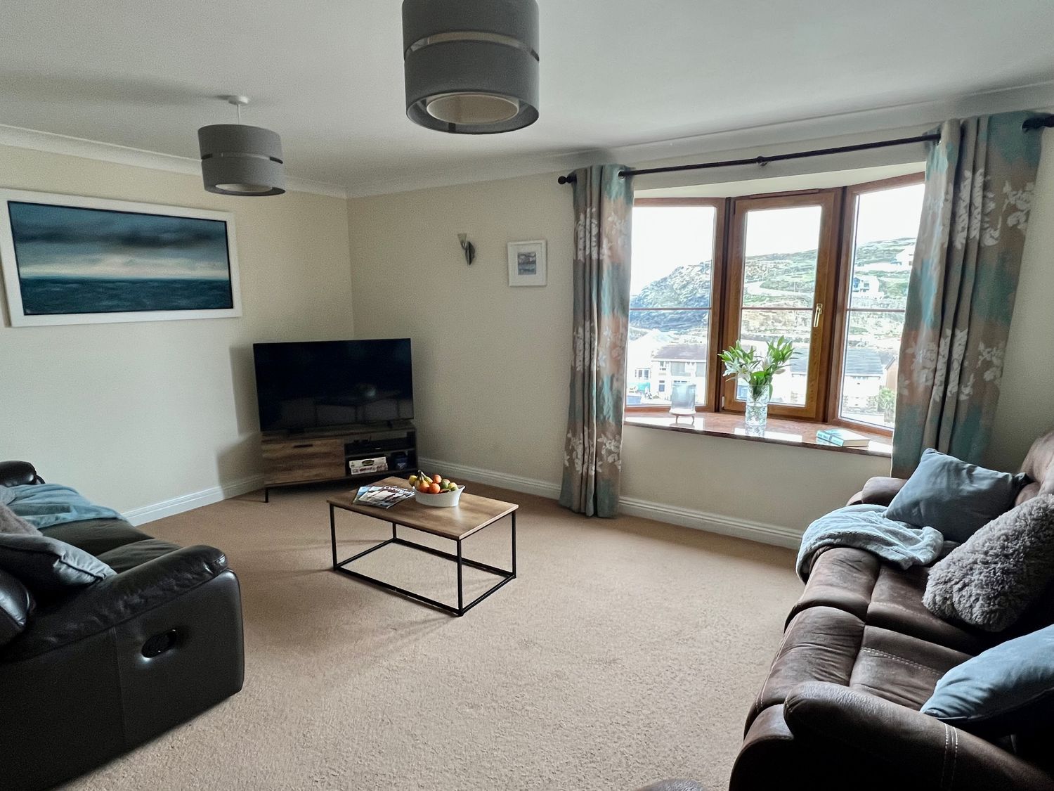 A living room with two sofas a coffee table a television and a window with curtains at Curnows in Portreath