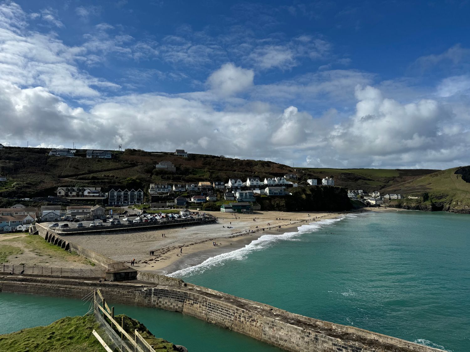 A coastal village with a sandy beach cars parked near buildings and hills in the background at Curnows Portreath