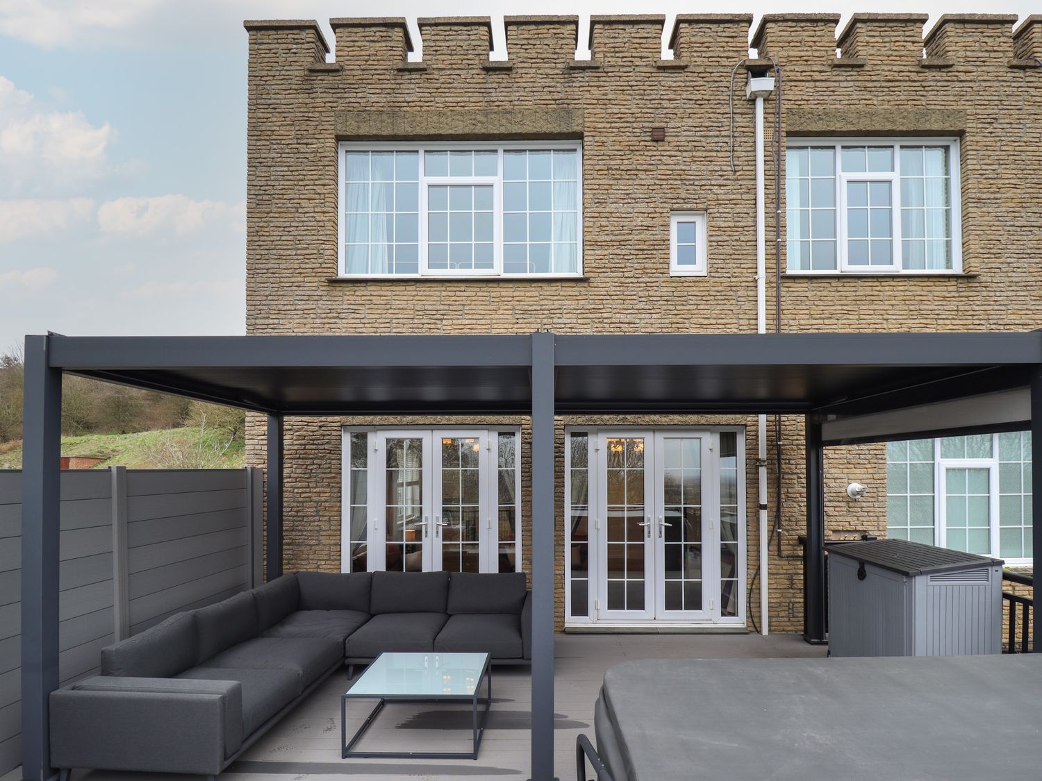 A patio area with gray sectional sofa and glass coffee table under a black pergola at Castle Top Haven in Nettleton Top near Caistor
