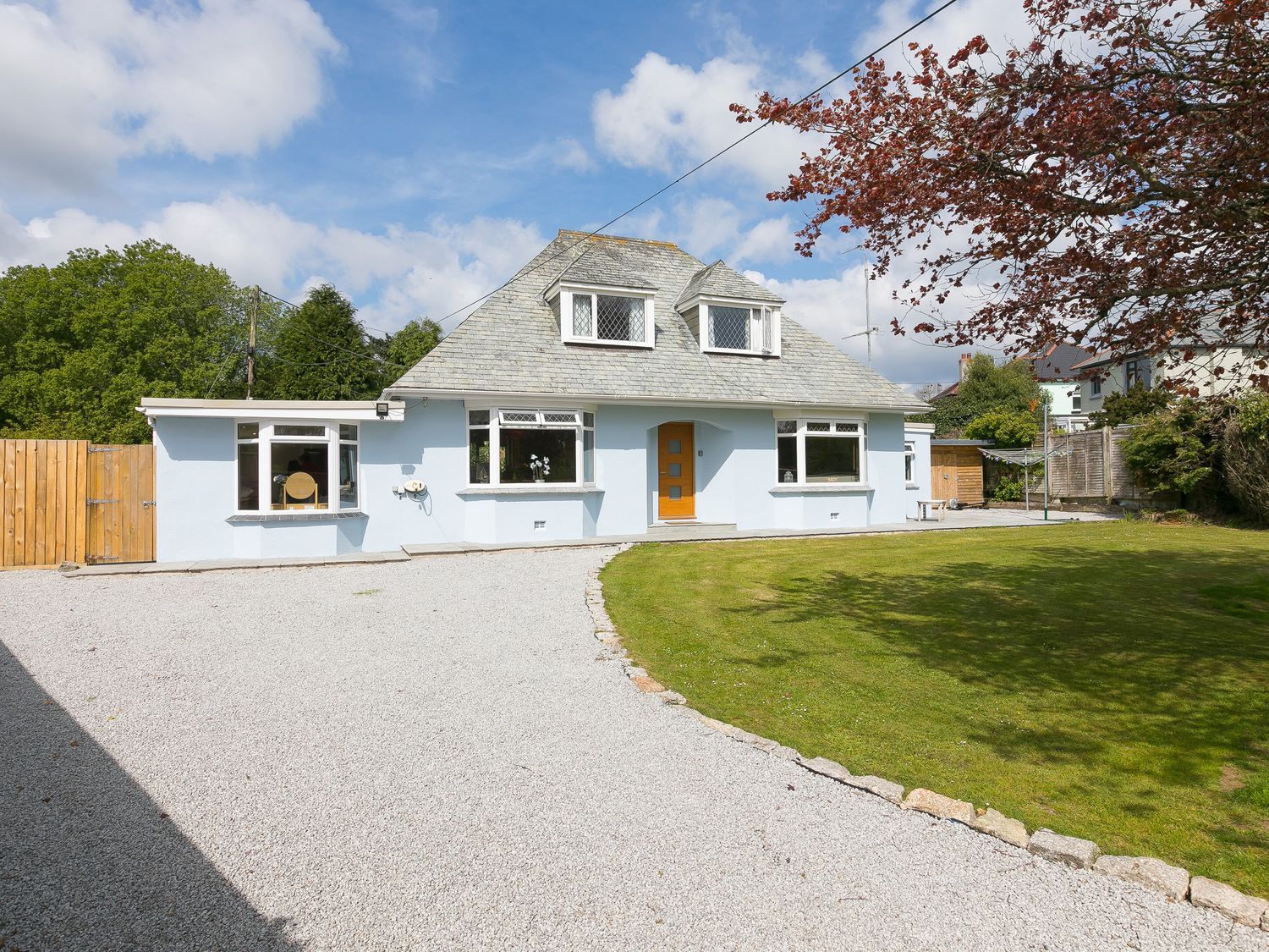 A house with a gravel driveway and a lawn with trees at Wyvern Four Cross near Penryn