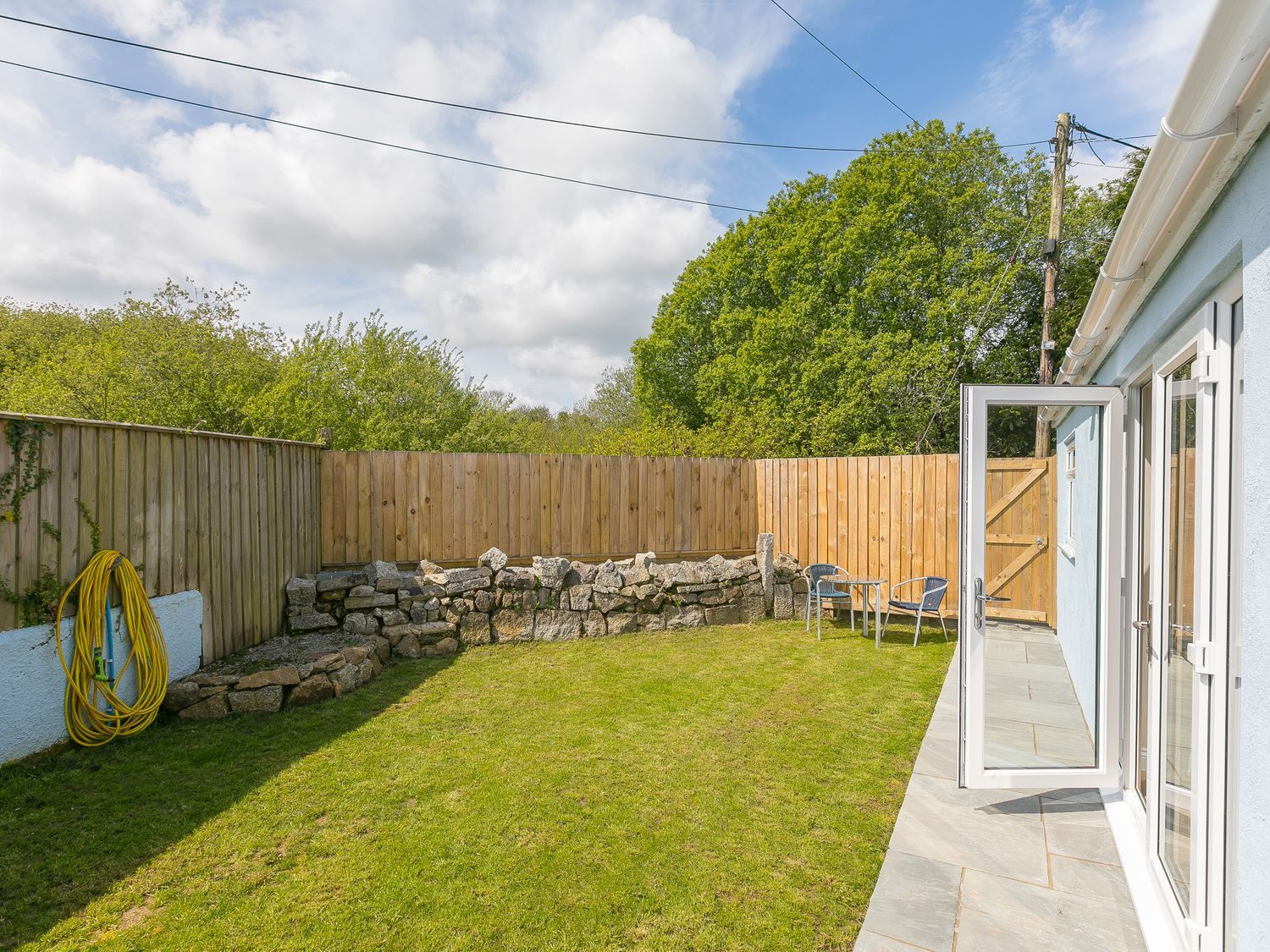A fenced backyard with grass stone wall table and two chairs outside a house at Wyvern Four Cross near Penryn