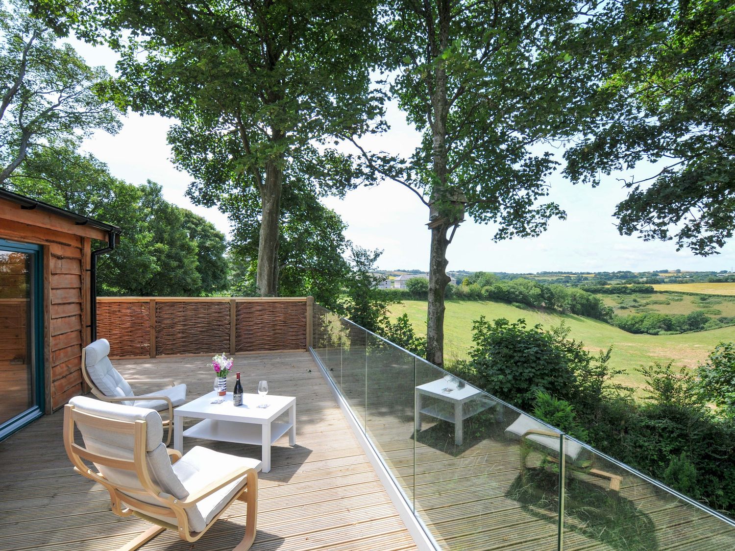 A deck with chairs and a table overlooking fields at Owl Lodge in Menheniot