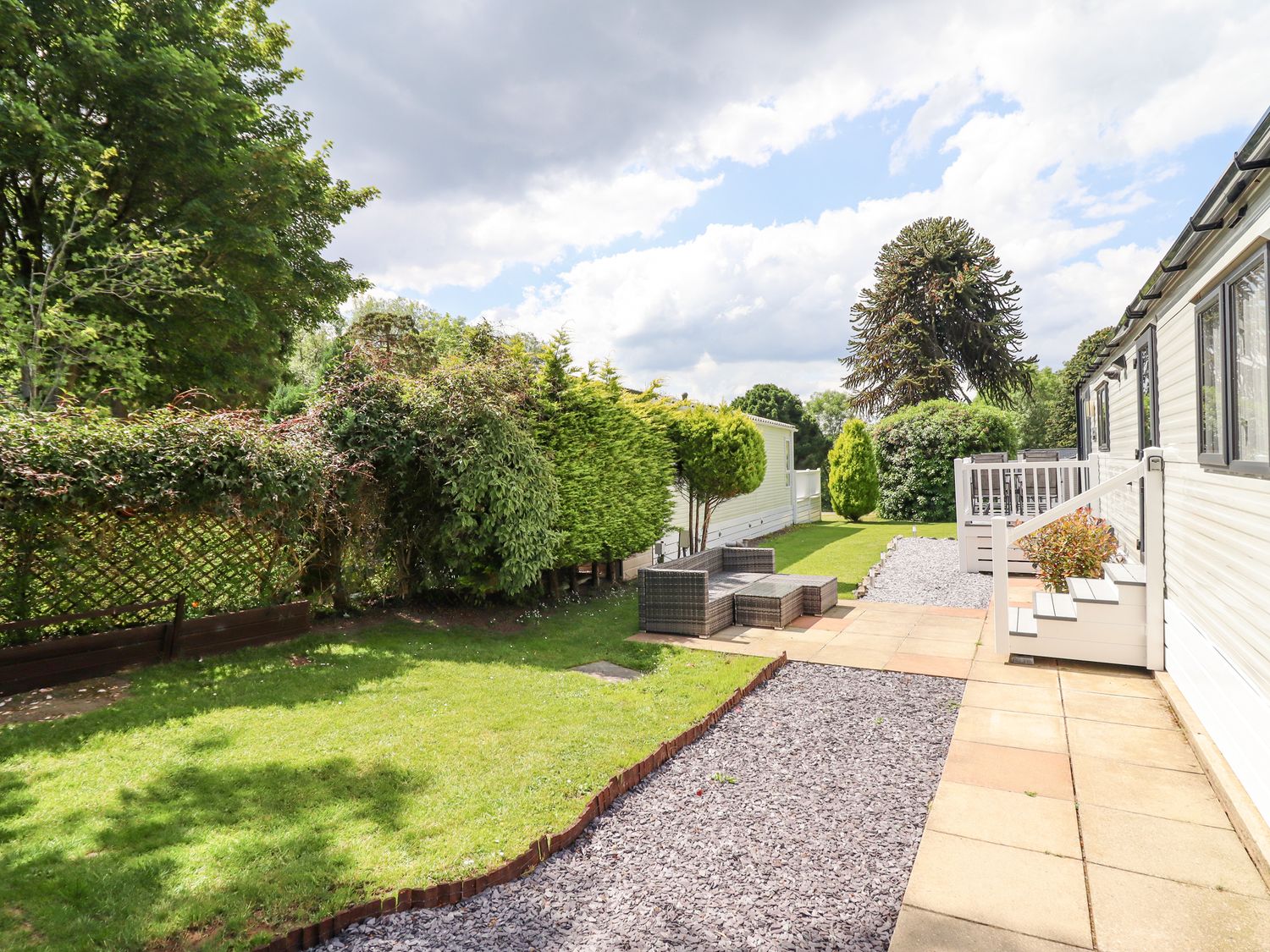 An outdoor area with patio flooring seating and grass next to white mobile homes at Woodlands Lodge in Bontuchel near Ruthin