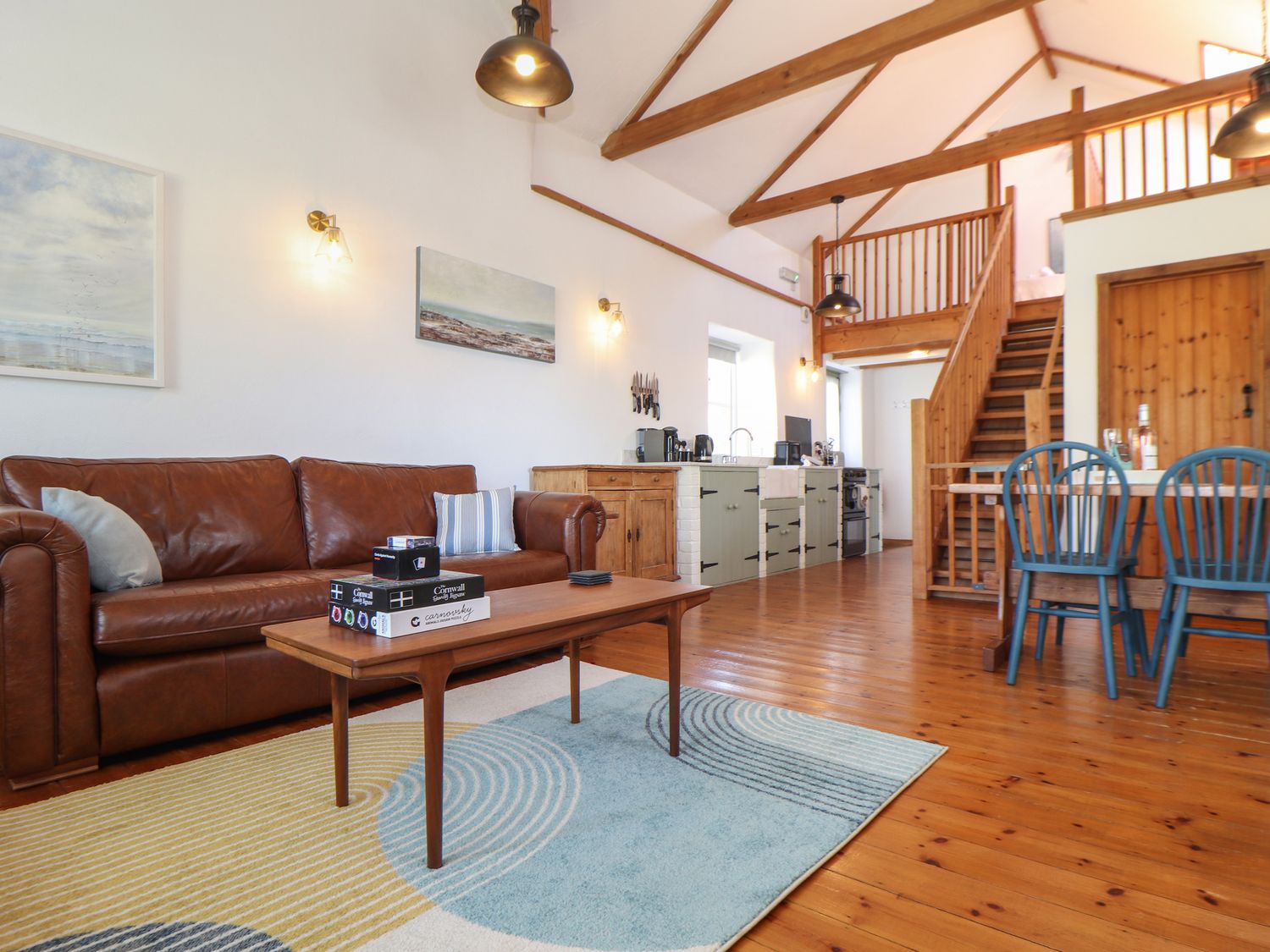 An open living area with a brown leather sofa a wooden coffee table and a kitchen in the background at Joes Barn in Mullion