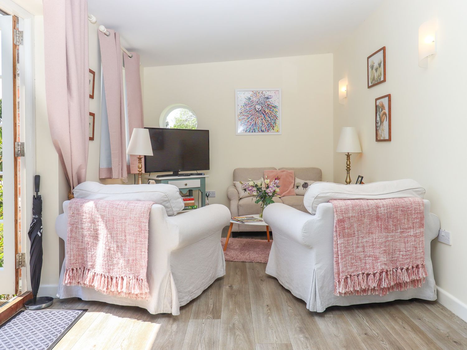 A living room with two white armchairs with pink throws facing a beige sofa with cushions and a coffee table at Sunset Cottage Swimbridge near Barnstaple