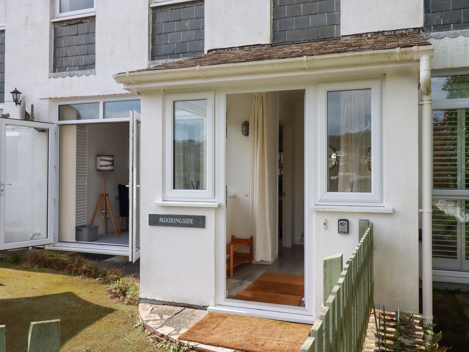Exterior entrance of a white building with open glass doors and a small garden area at Mooringside in Penpol near Carnon Downs