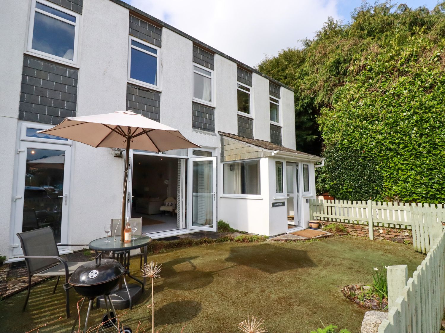 A backyard with a patio table umbrella chairs and a barbecue grill outside a two story house at Mooringside Penpol near Carnon Downs