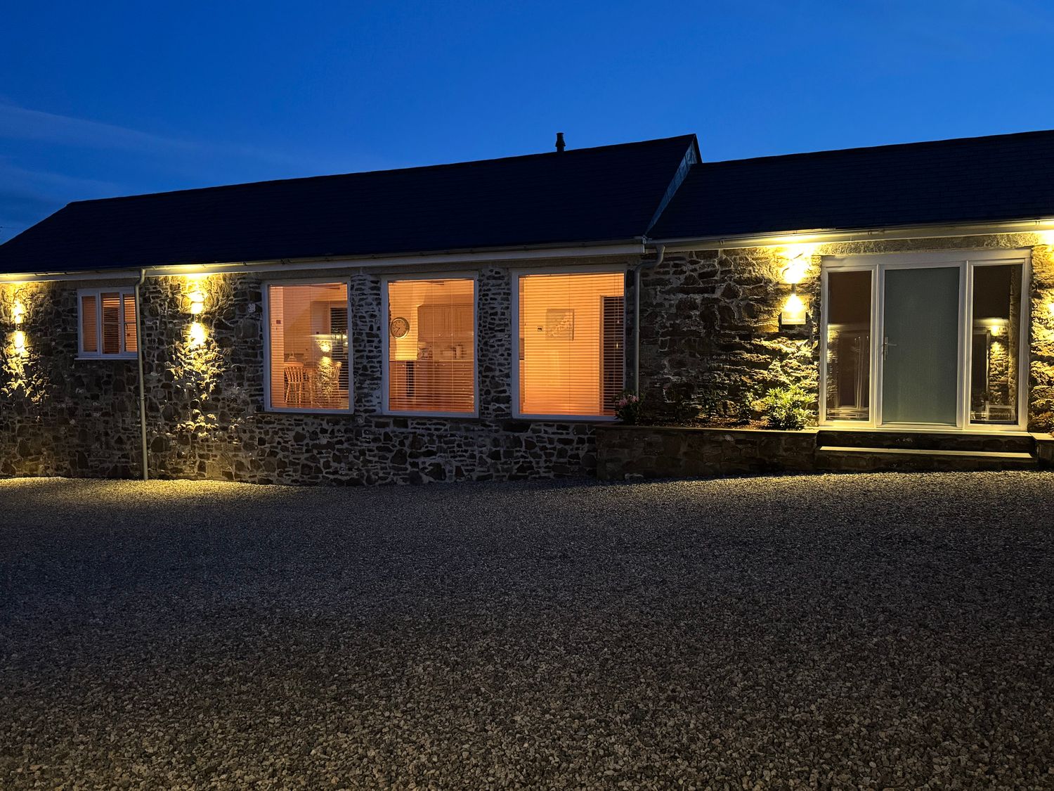 A stone building with lit windows and exterior lights at Old Orchard Barn St Mellion near St Dominick