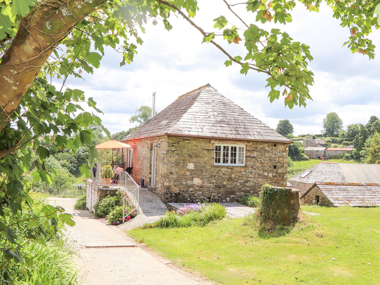 A stone cottage with a slate roof surrounded by greenery and trees at Skiber Coombe in Bray Shop near Launceston