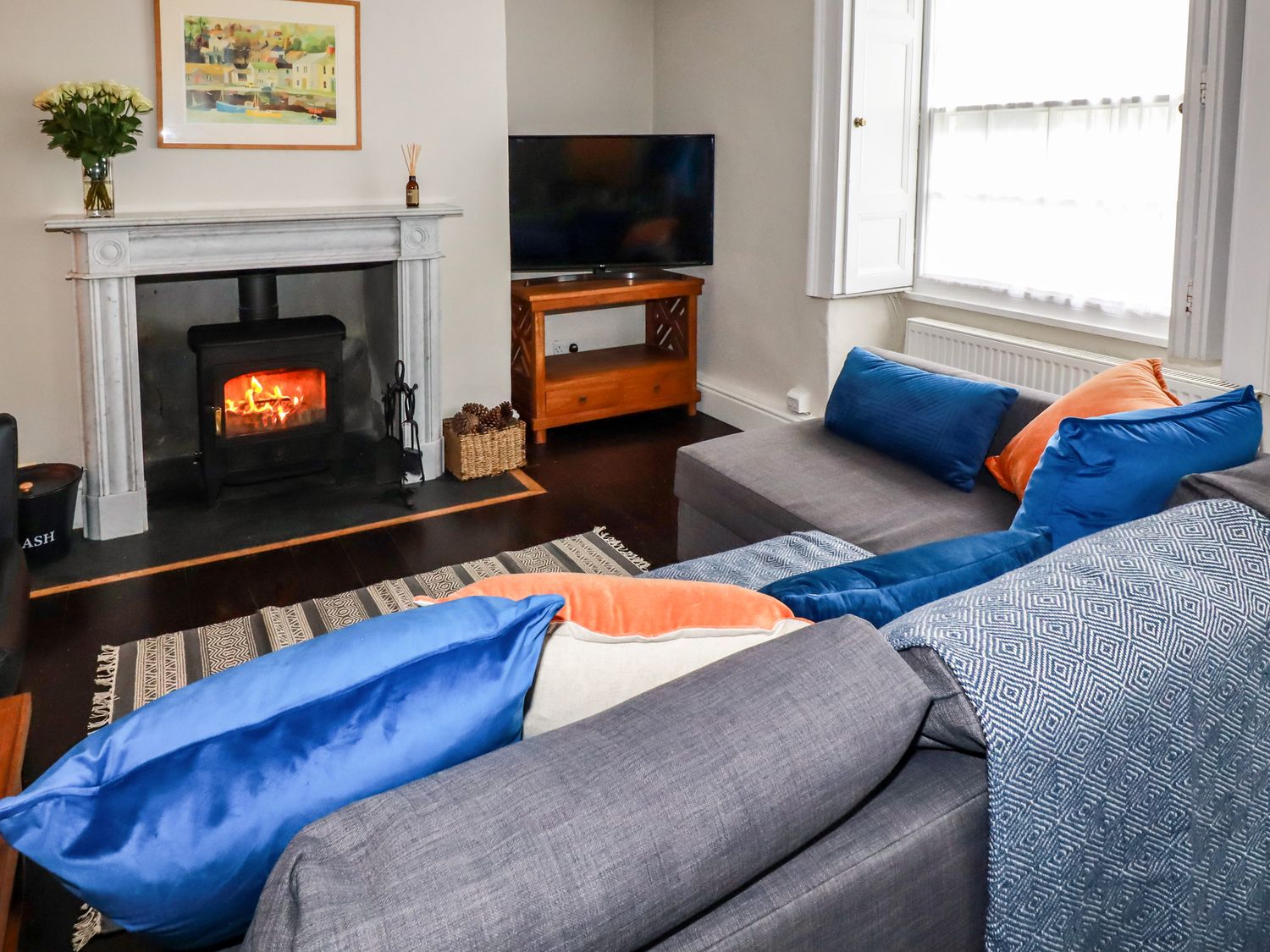 A living room with a fireplace wood burning stove and a grey sofa with blue and orange cushions at Carew House Cottage in St Day