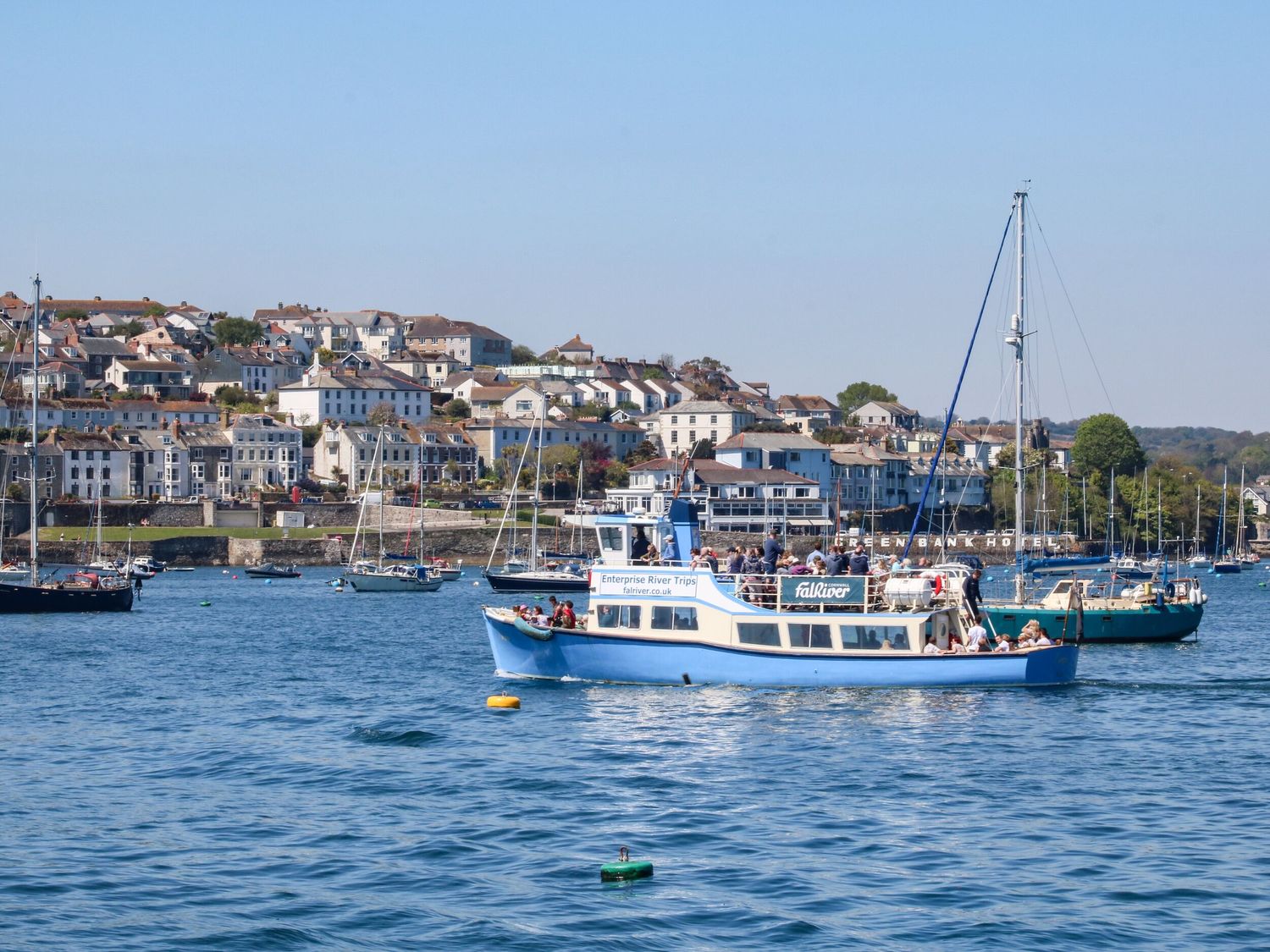 A boat with people on a body of water near a town with houses and other boats in the background at Carew House Cottage in St Day