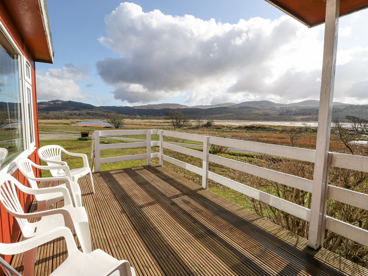 A wooden deck with white plastic chairs overlooking fields and hills at Lochead Chalet in Achahoish near Lochgilphead