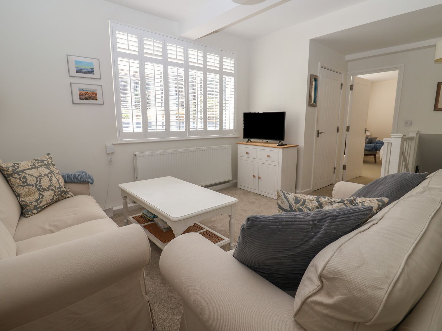 A living room with two beige sofas pillows a white coffee table and a small white TV cabinet at 16 Church Street Lyme Regis