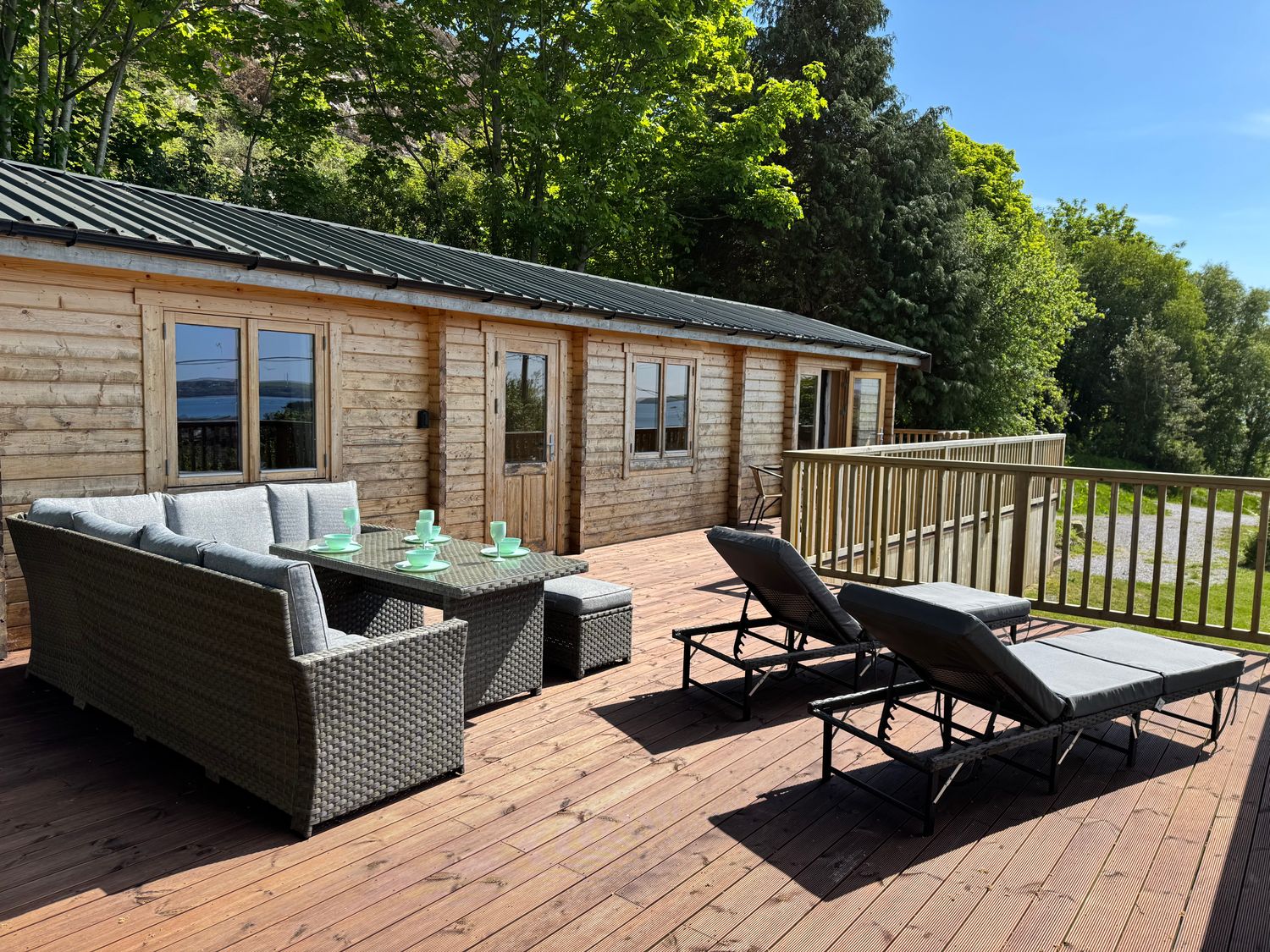 A wooden patio with outdoor furniture including a sofa set with a table and two lounge chairs at Northwood Lodge in Llanbedrog
