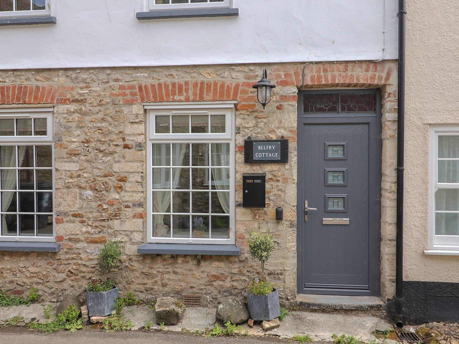 A front view of a cottage with stone walls and windows at Belfry Cottage in Colyton