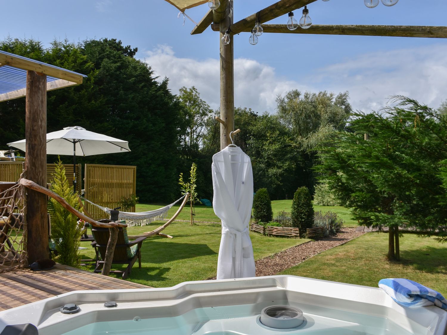 An outdoor area with a hot tub a wooden deck chairs hammock and umbrella at Burr 2 Shepherds Hut in Swimbridge near Barnstaple