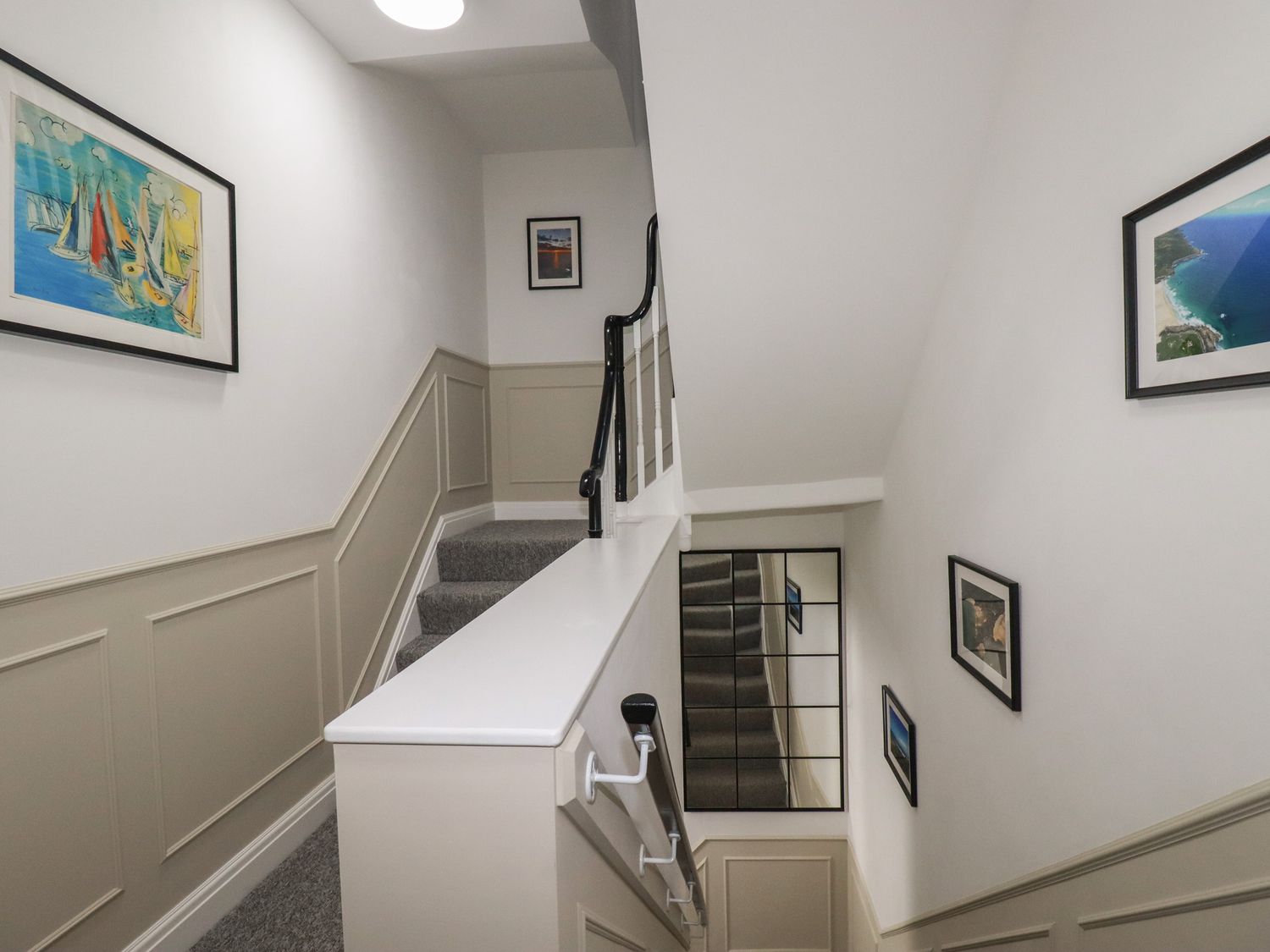 A staircase with framed pictures on the walls and a mirror at Kerensa in St Austell