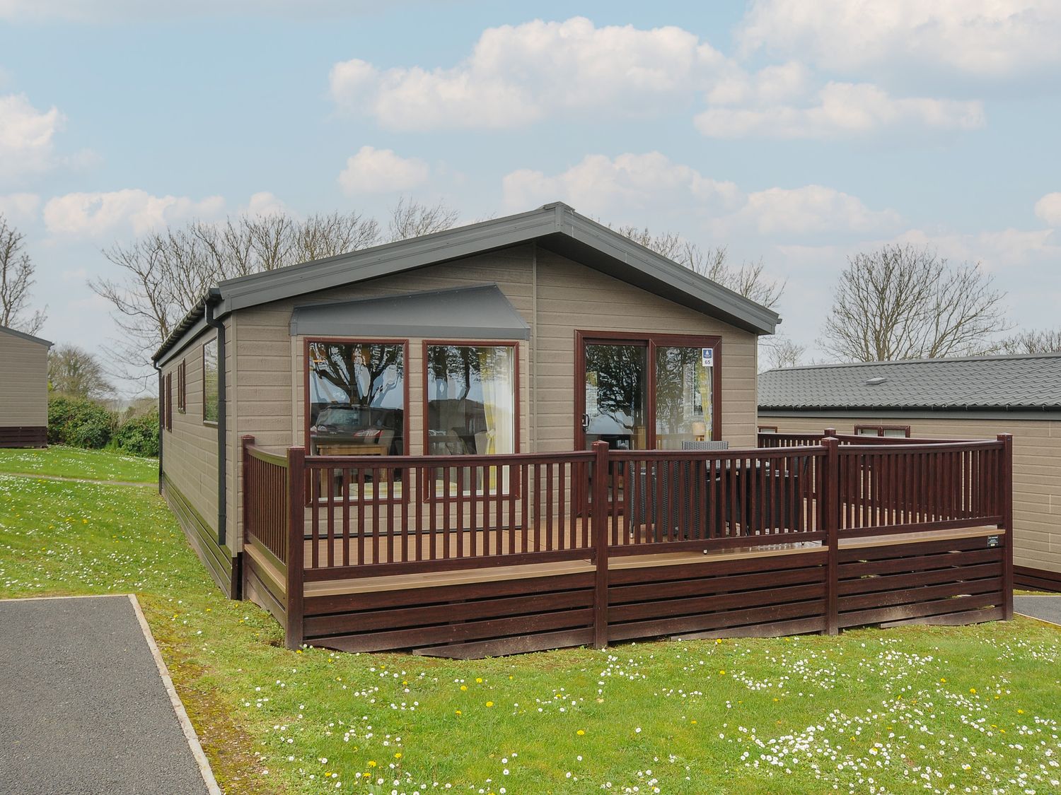 A single-story wooden cabin with a fenced front porch on a grassy area at Lodge 66 at Riviera Bay Coastal Retreat in Brixham