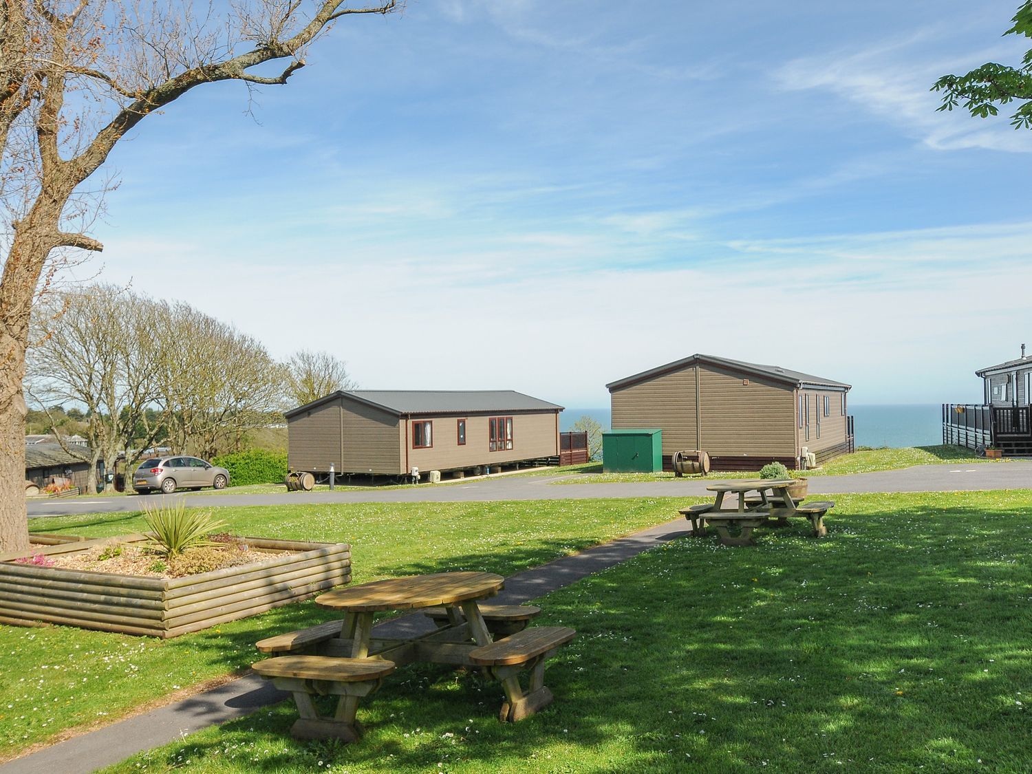 A grassy area with picnic tables and wooden cabins with a view of the sea at Lodge 55 at Riviera Bay Coastal Retreat in Brixham
