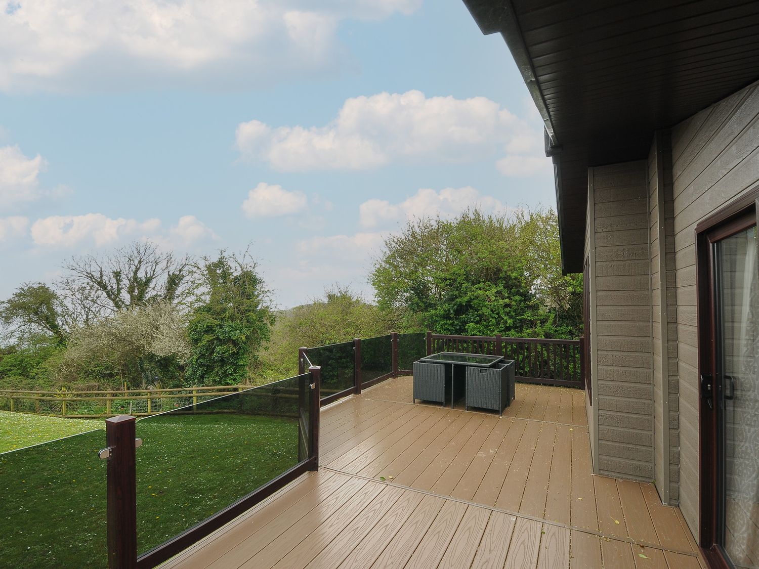 A wooden deck with glass railing and outdoor furniture next to a house at Lodge 59 at Riviera Bay Coastal Retreat Brixham