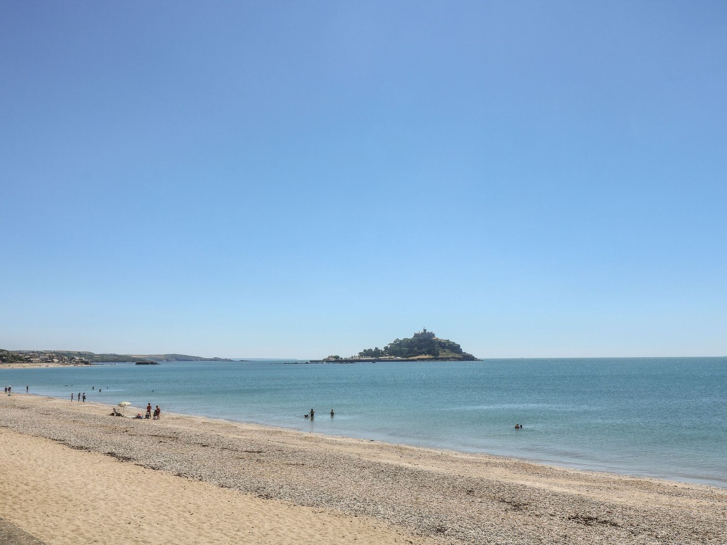 A sandy and pebbly beach with people near the water and a small island with buildings in the distance at Little Wren Cottage in Marazion