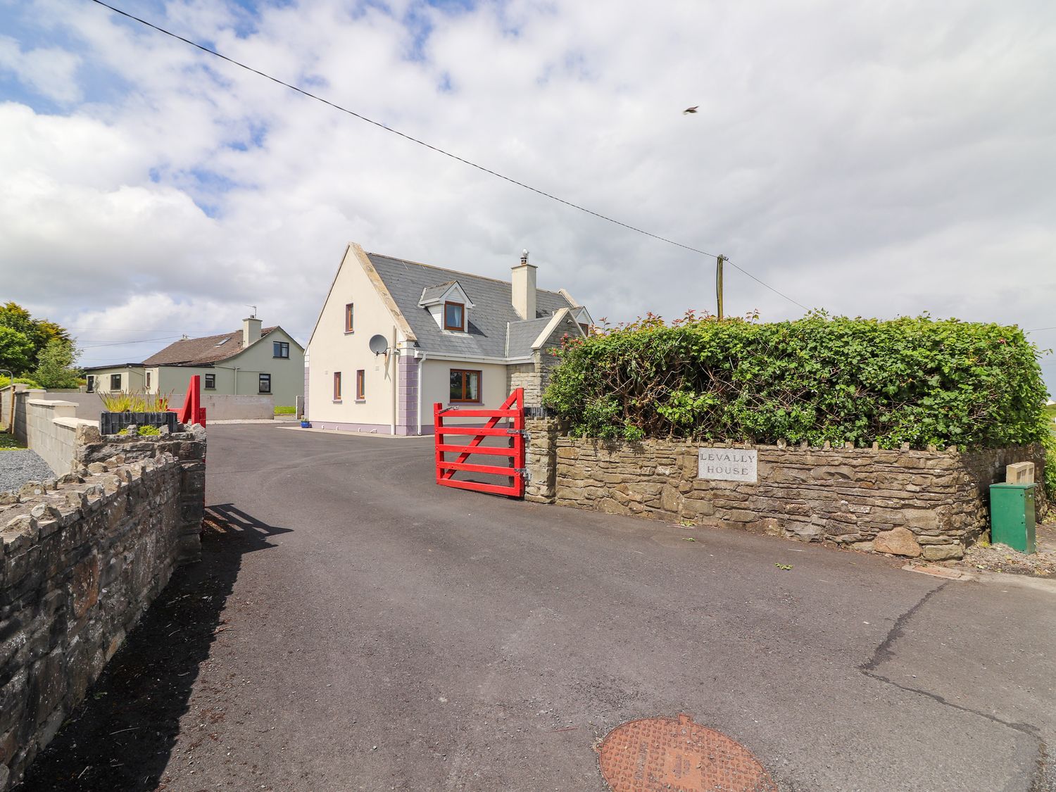 A paved driveway leading to a house with a red gate and a stone wall with greenery at Levally House Mountrivers Bridge near Doonbeg County Clare