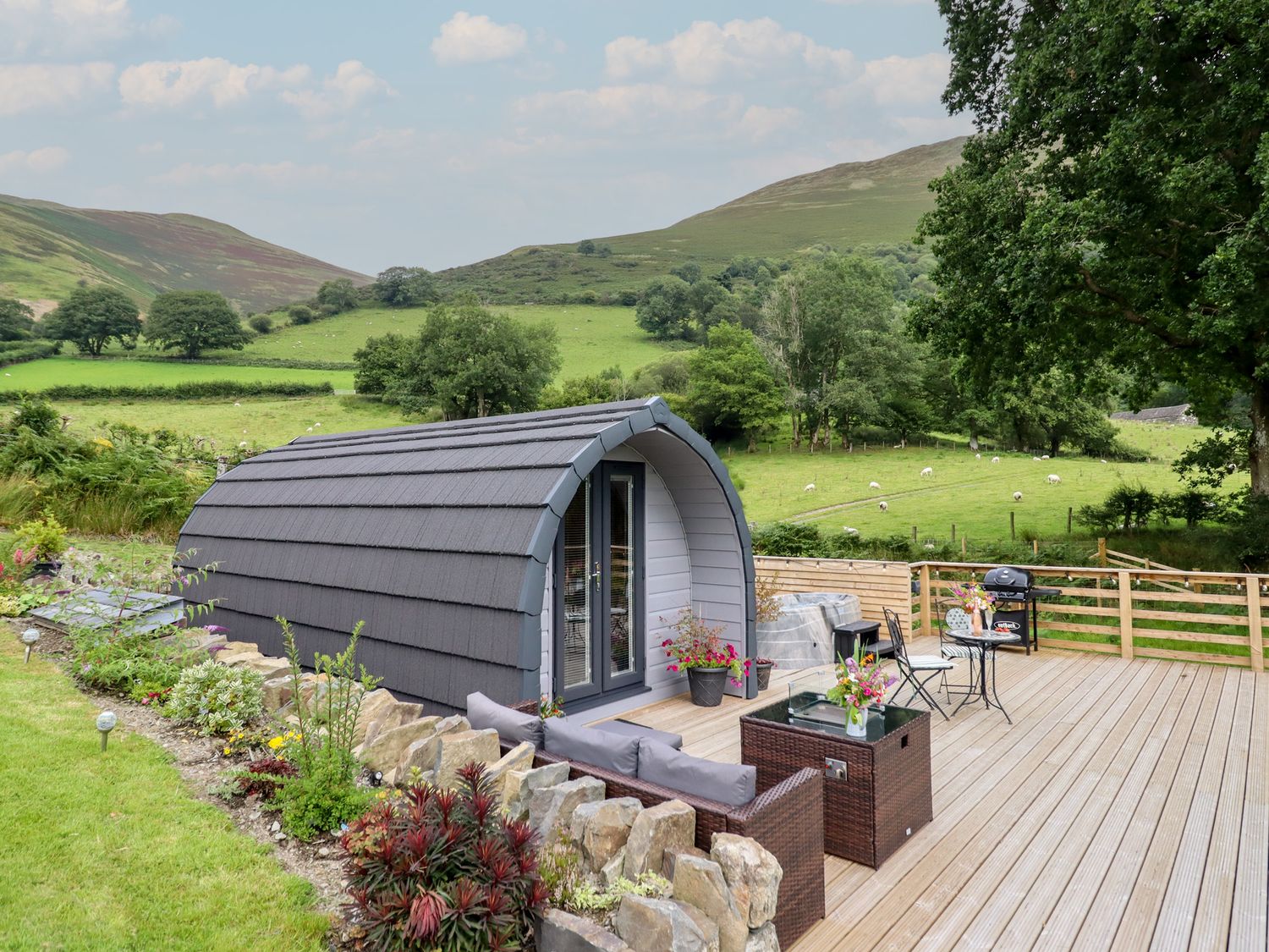 A cabin with a deck and furniture near a green landscape at Caban Tirion in Dinas Mawddwy near Dolgellau