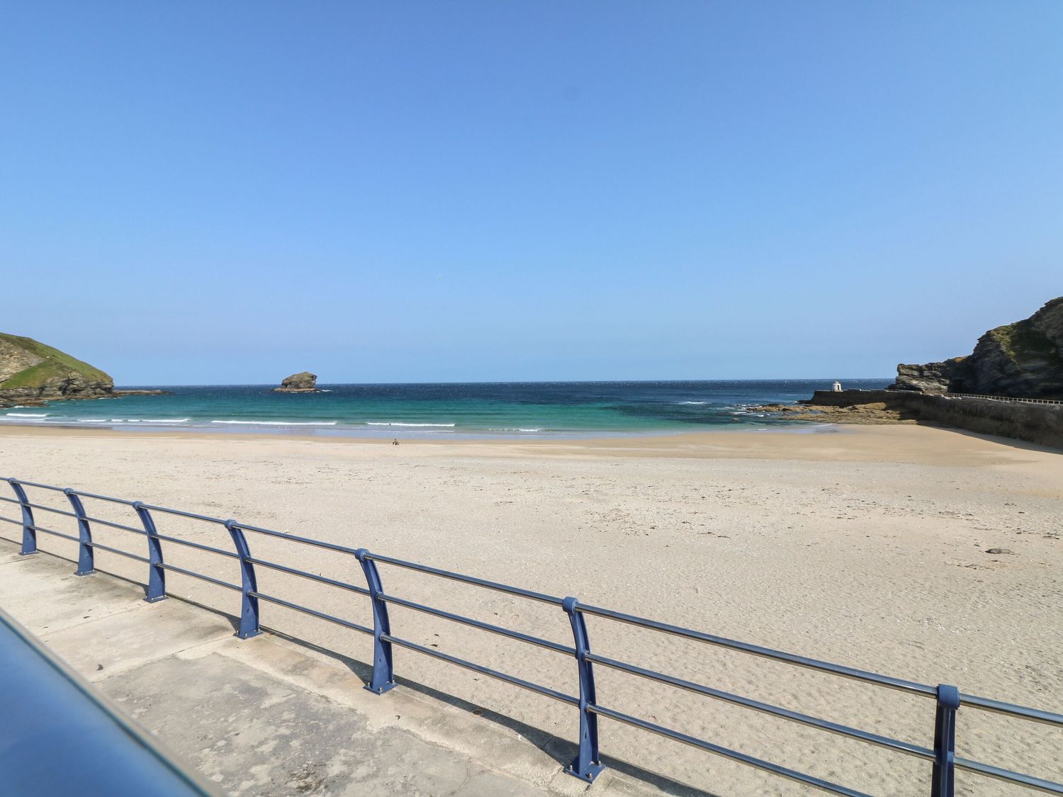 A sandy beach with a blue railing and a rock formation in the sea at Apartment above Garryglass in Portreath