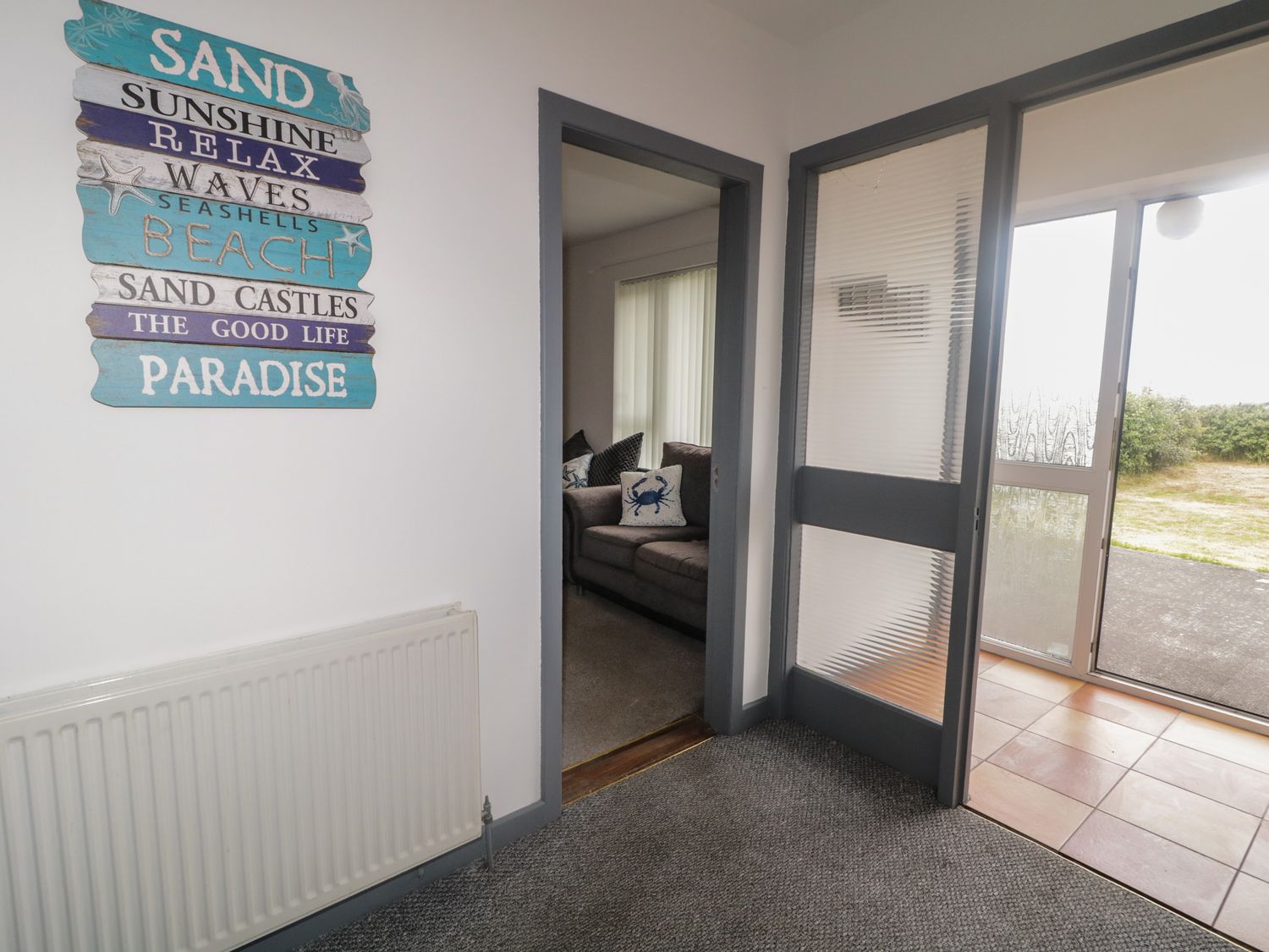 An entryway with a wall sign next to a door leading to a living room with a gray couch and a door leading outside at The Island's View in Gortahork County Donegal