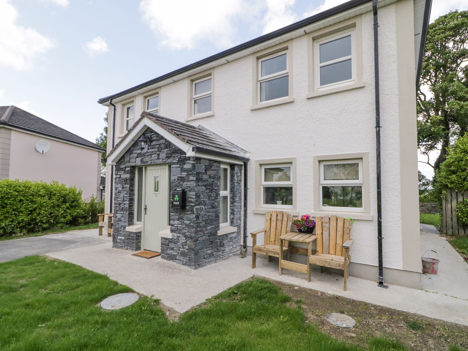 A white two-story house with stone porch and wooden bench with flowers outside at Stoneywood Culdaff County Donegal