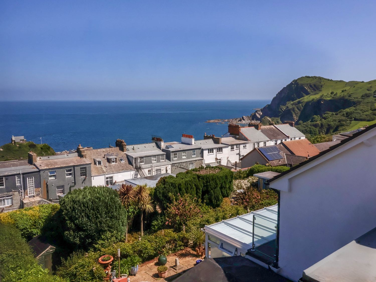 A coastal view with houses and greenery overlooking the sea and cliffs at Combe View in Ilfracombe