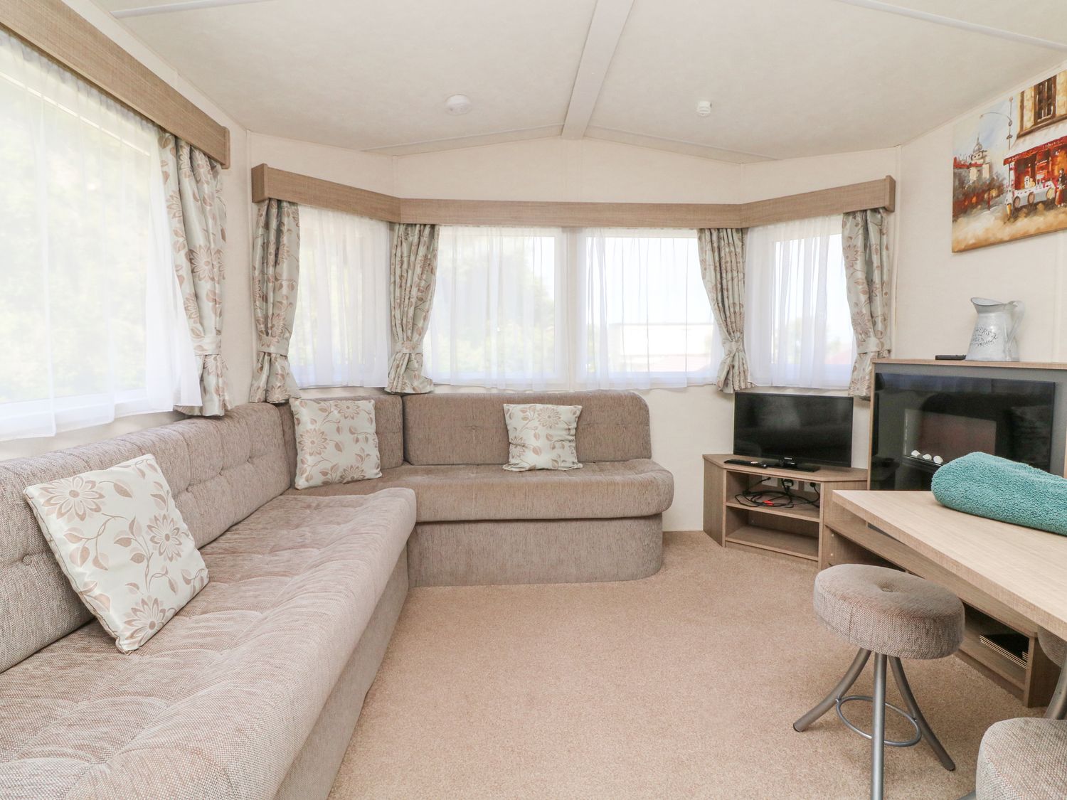 A living room with a beige sofa corner cushions small television and stool at 23 Manleigh Park in Combe Martin