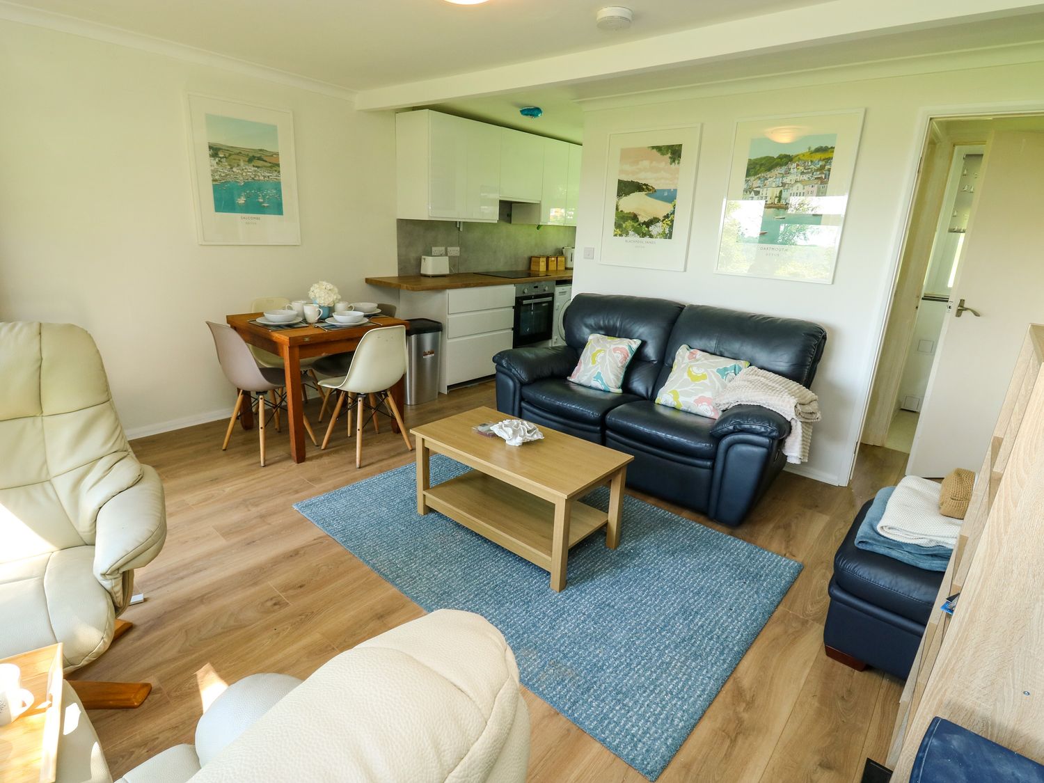 A living room with a blue sofa a wooden coffee table and a dining table next to a kitchen area at 61 Norton Park in Dartmouth