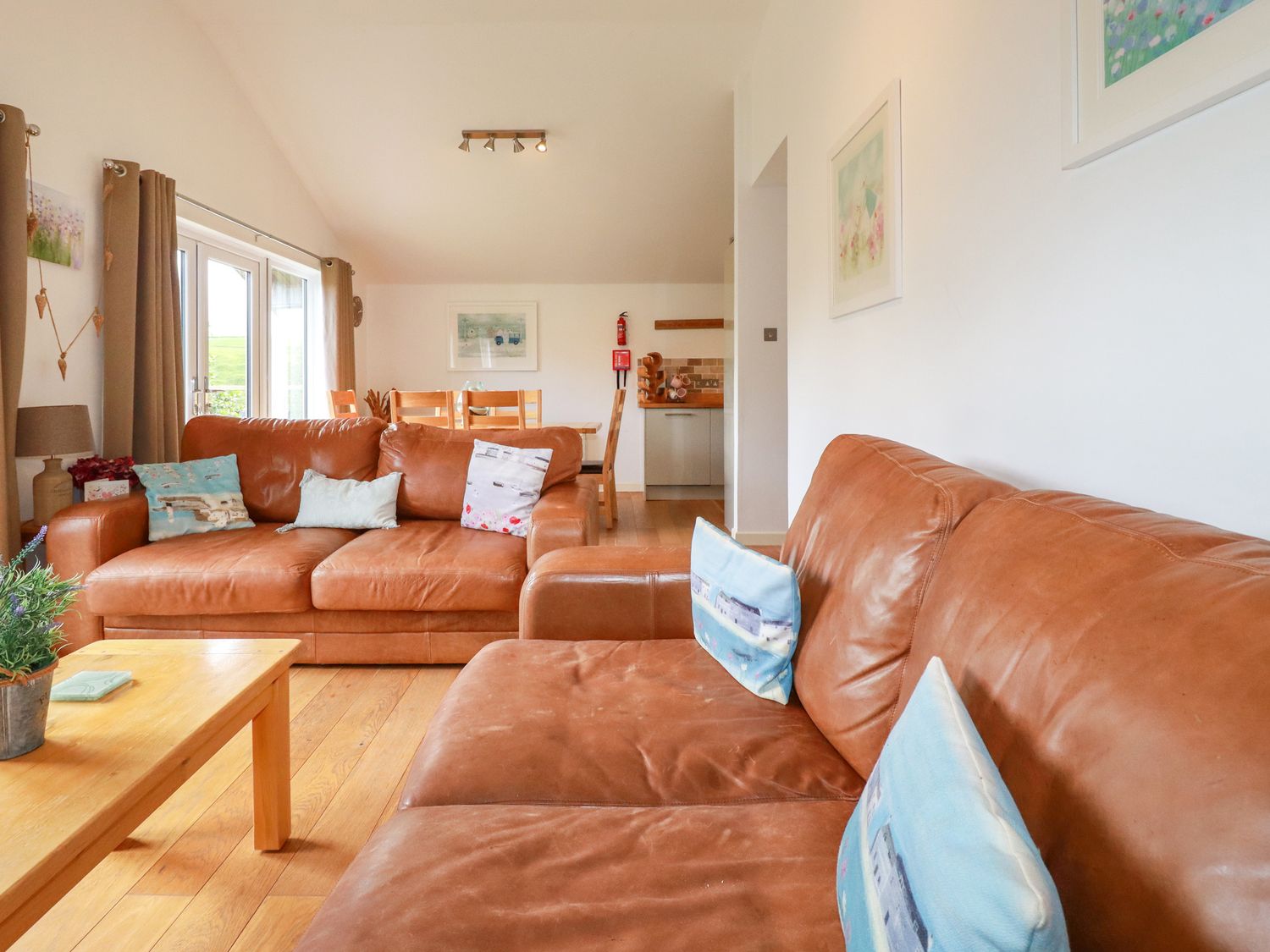 A living room with two brown leather sofas a wooden coffee table and dining table at 3 Lake View in Lanreath