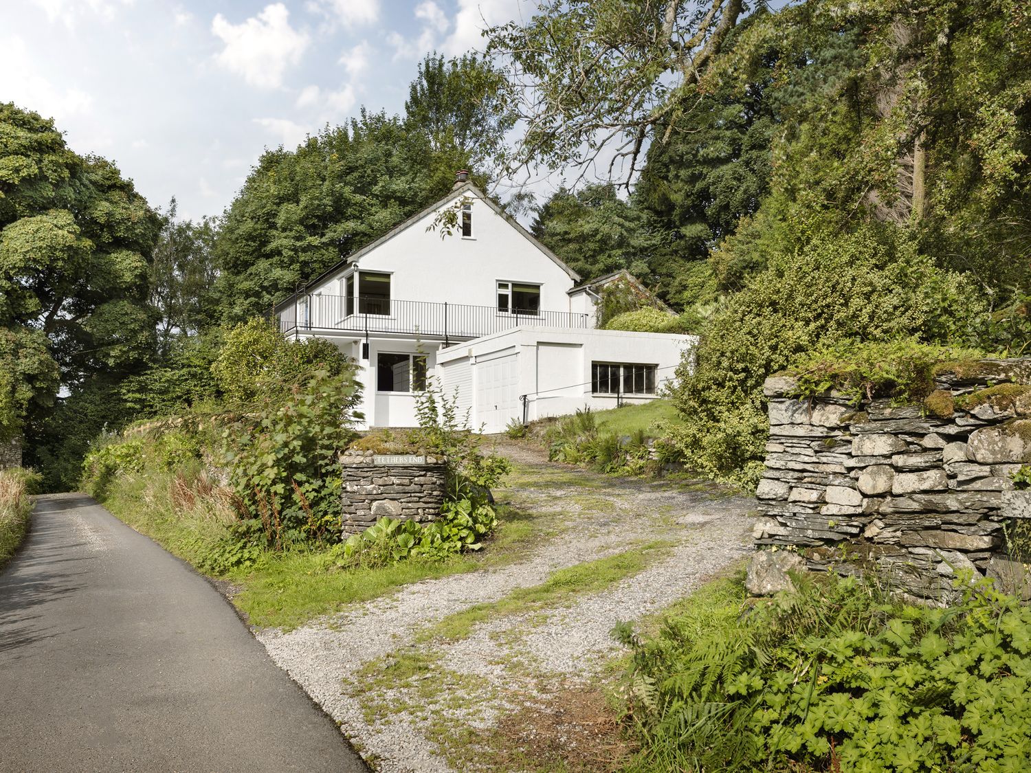 A house surrounded by trees and a gravel driveway at Tethers End in Lindeth near Bowness-On-Windermere