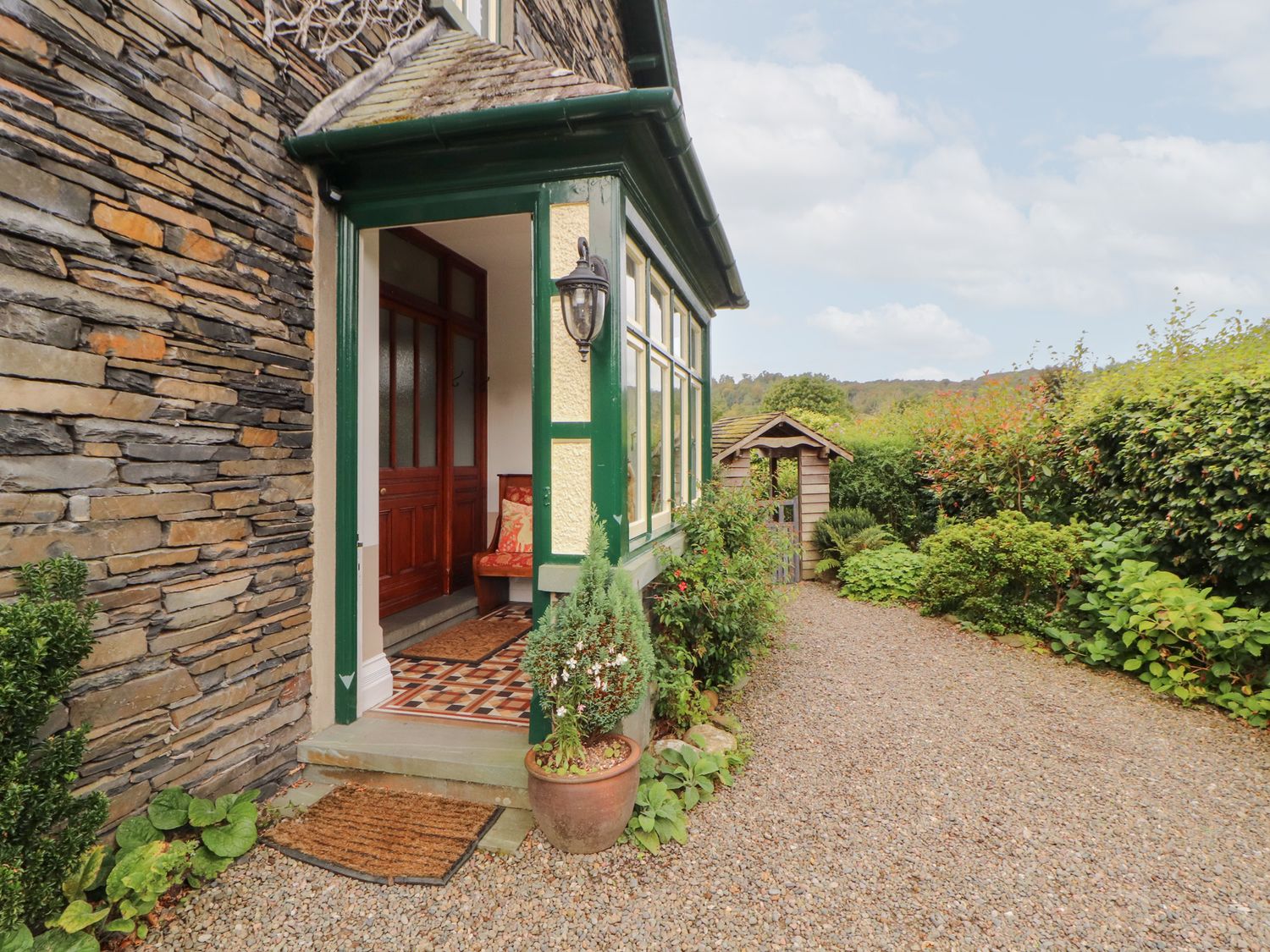 An entrance with a stone wall, door, and garden path at Bracken Howe in Ambleside