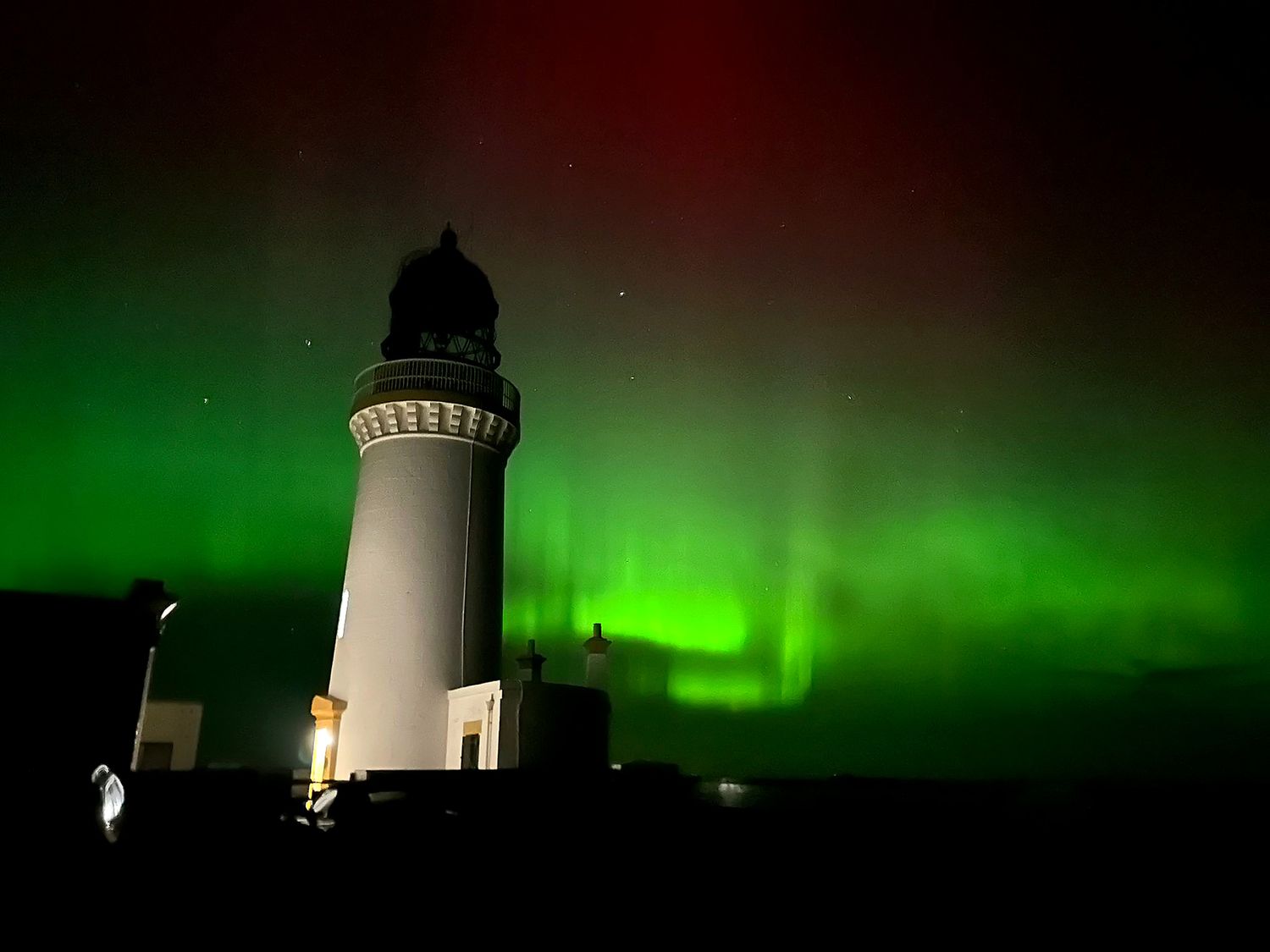 A lighthouse under aurora borealis at The Lighthouse Keepers Cabin Noss Head near Wick Caithness