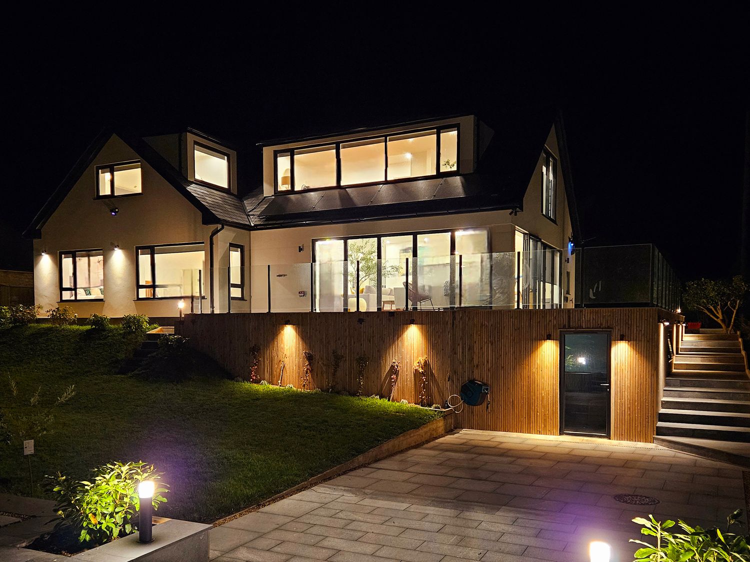 A modern house at night with lit windows outdoor lights a patio and stairs leading up to the entrance at Mayflower Mevagissey
