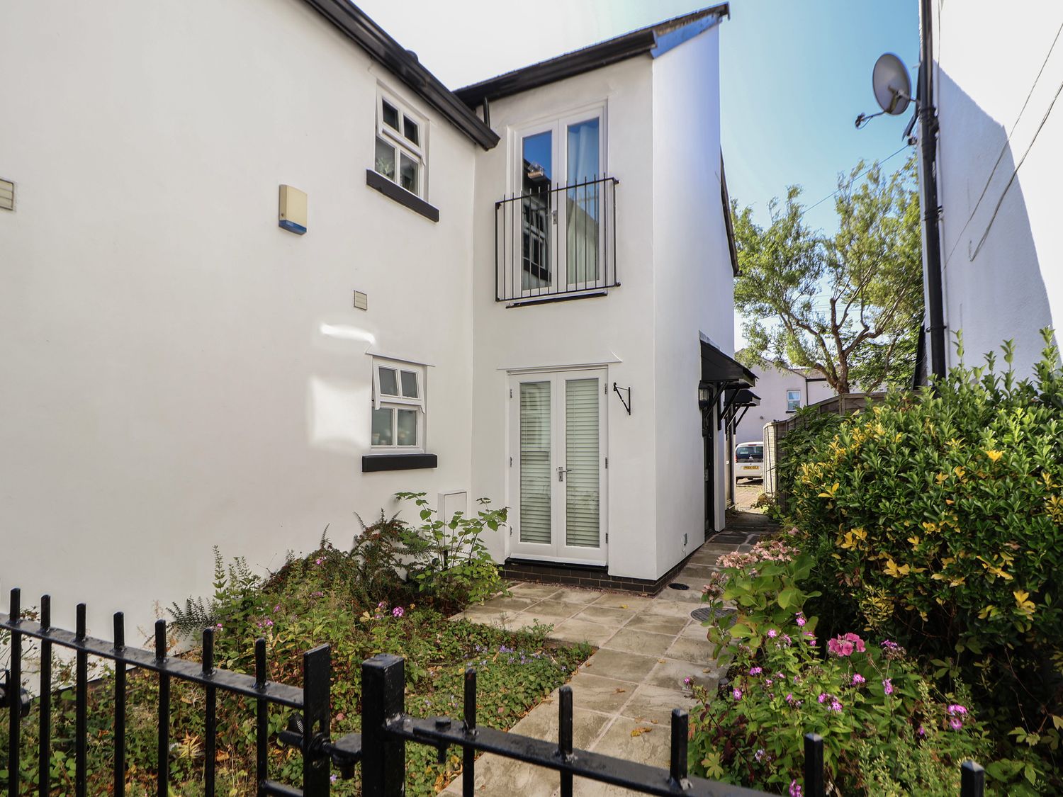 The exterior of a white building with black trim near a paved pathway and garden with plants and flowers at The Stocks in Newtown-le-Willows