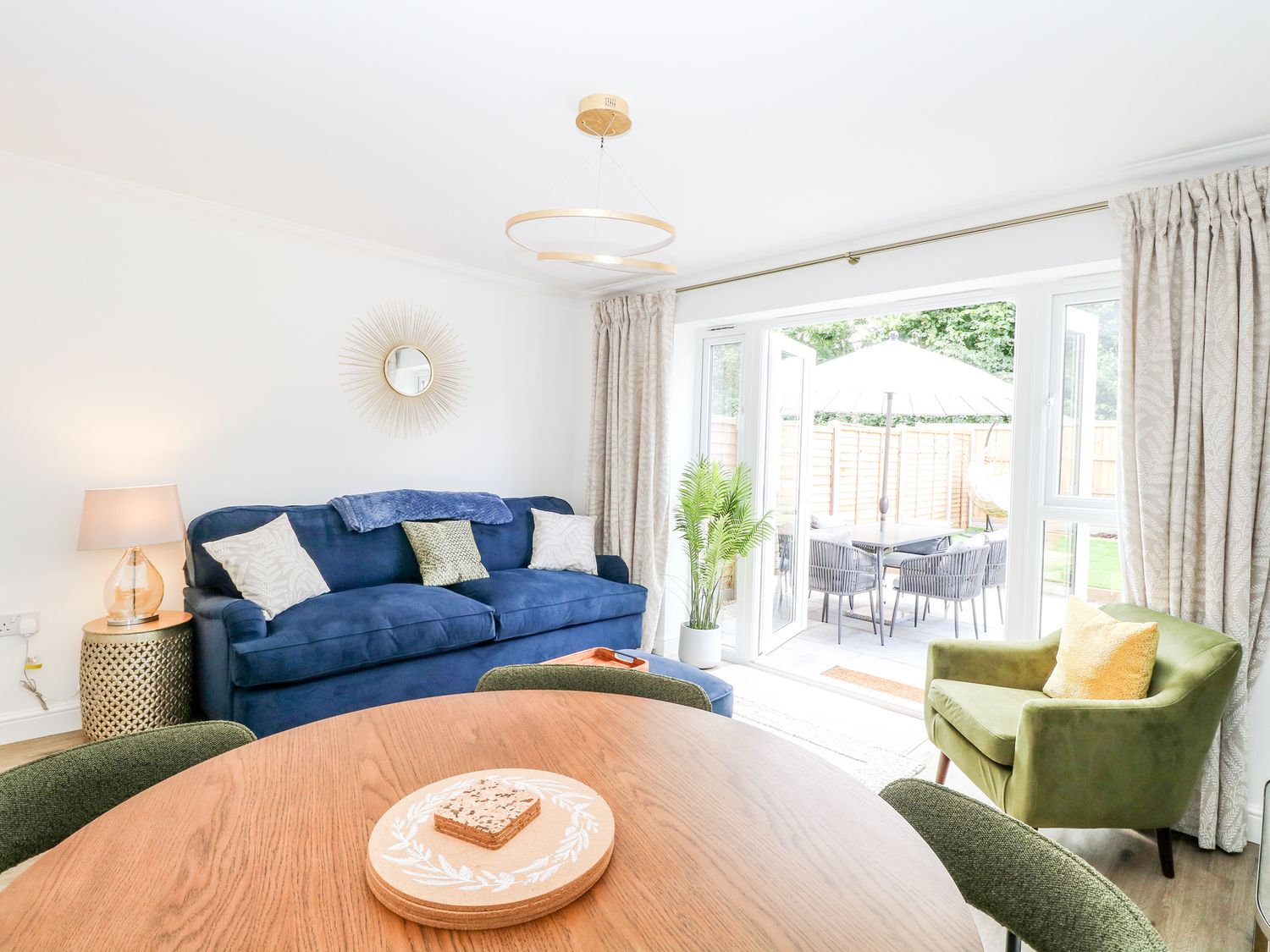 A living room with a blue sofa and green armchair next to glass doors opening to a patio at Pine Cottage in Wrentham