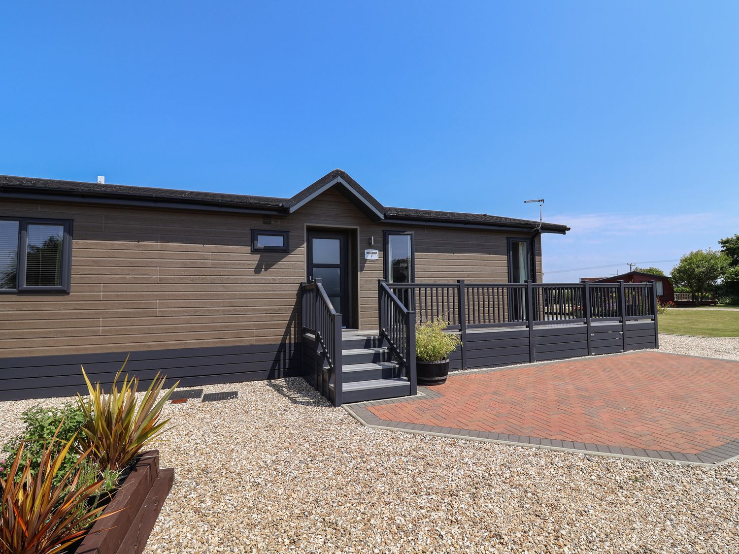 An exterior view of a single-story wooden lodge with stairs and a railing at Hazelwood 2 in Pinewood near Lyme Regis